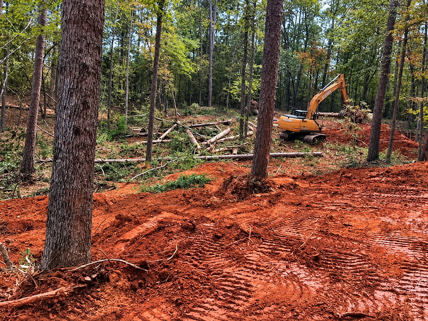 CASE excavator clearing timber and shaping red clay terrain on wooded site in Augusta, GA