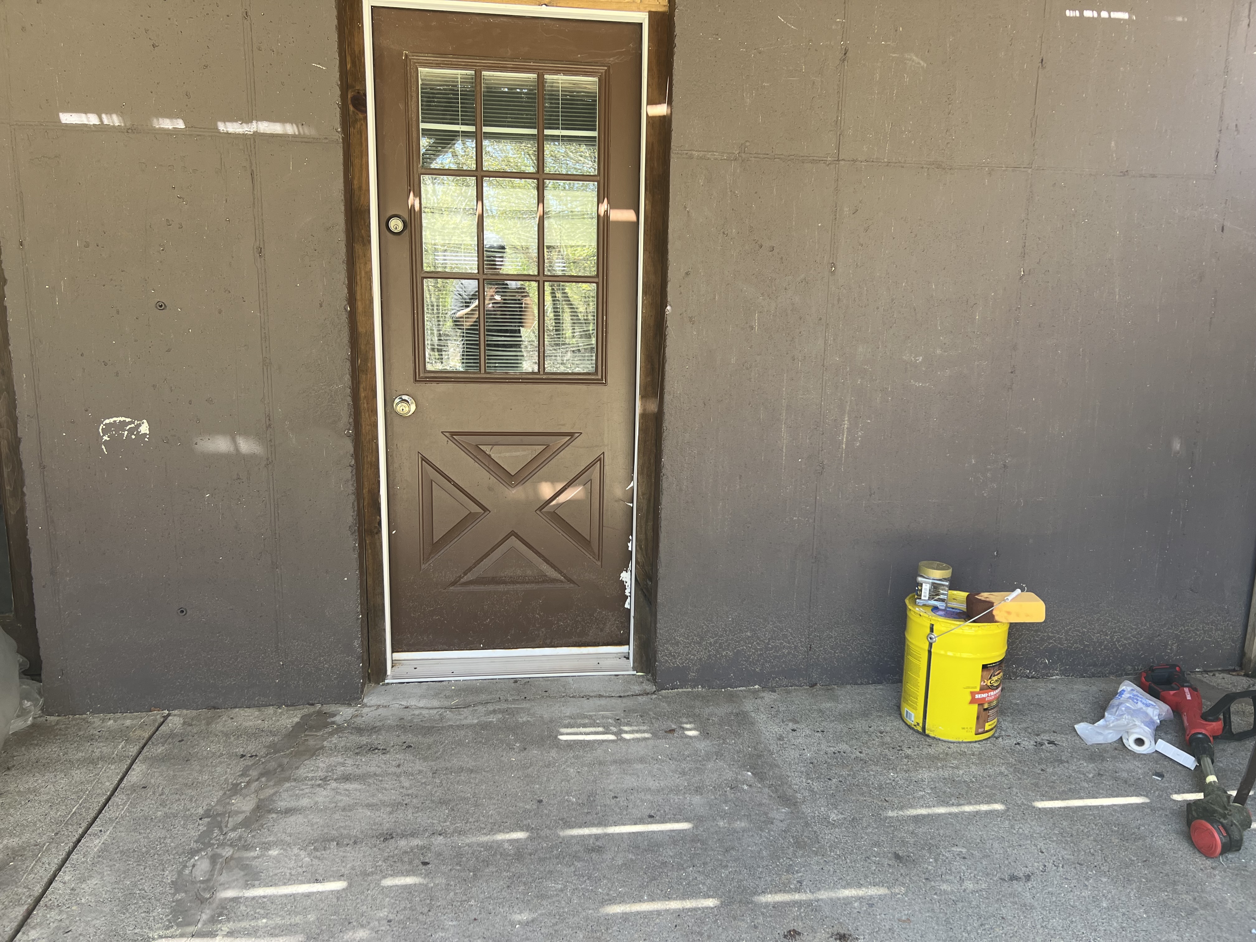 Poconos cabin before renovation — exterior door and concrete patio prep with paint supplies