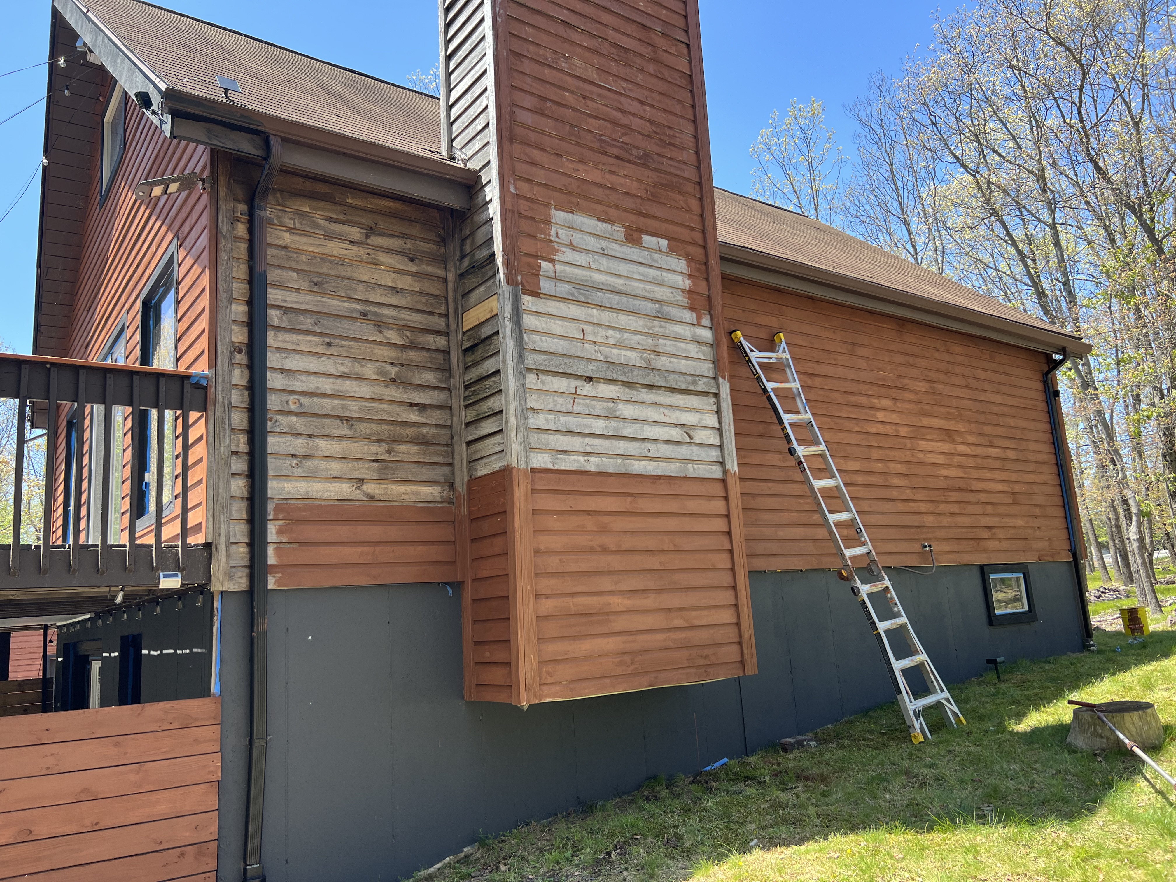 Poconos cabin in progress — side of cabin and chimney partially restained, showing before and after contrast