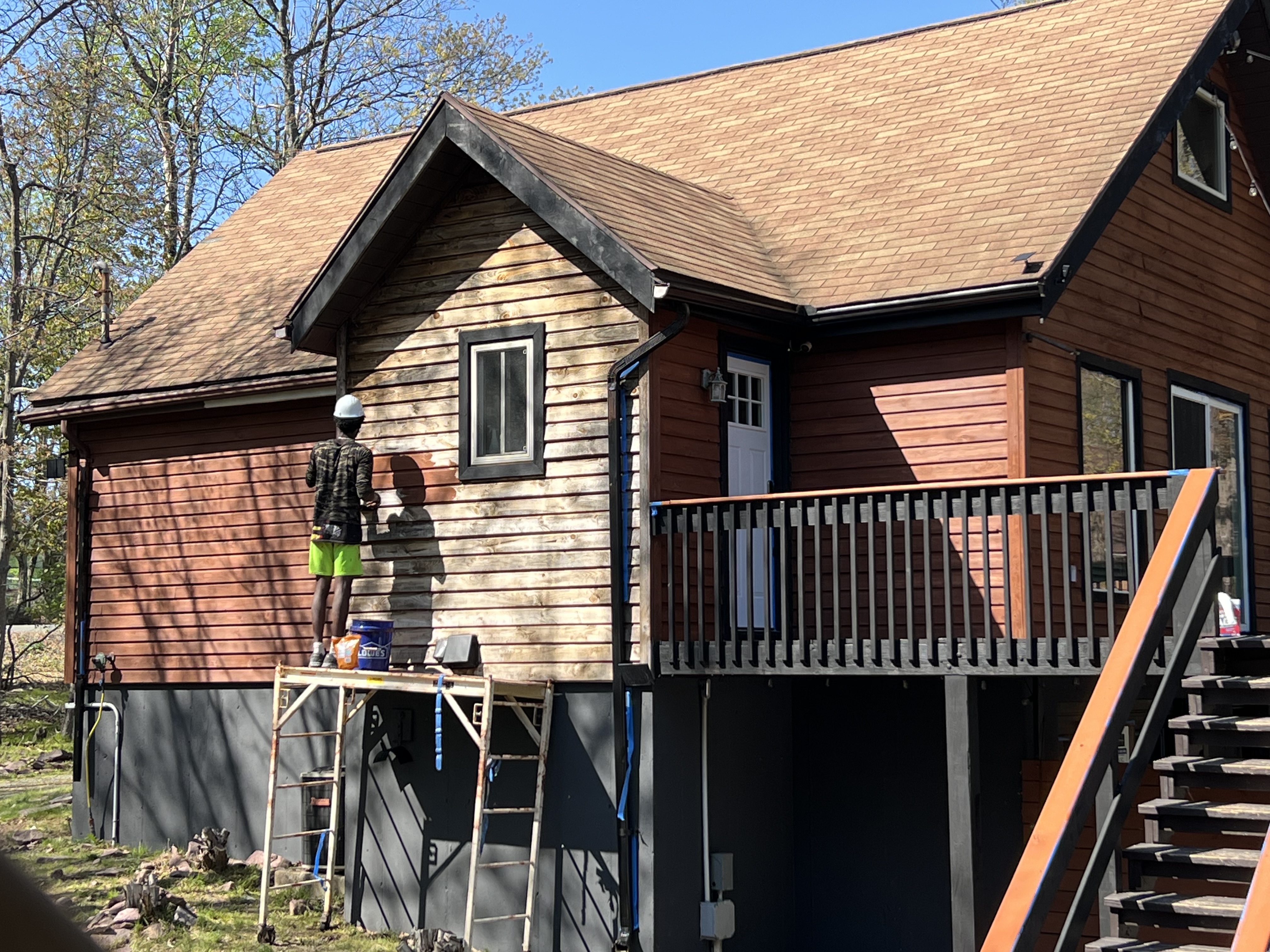 Poconos cabin in progress — crew member staining gable siding from rolling scaffold with clear blue sky