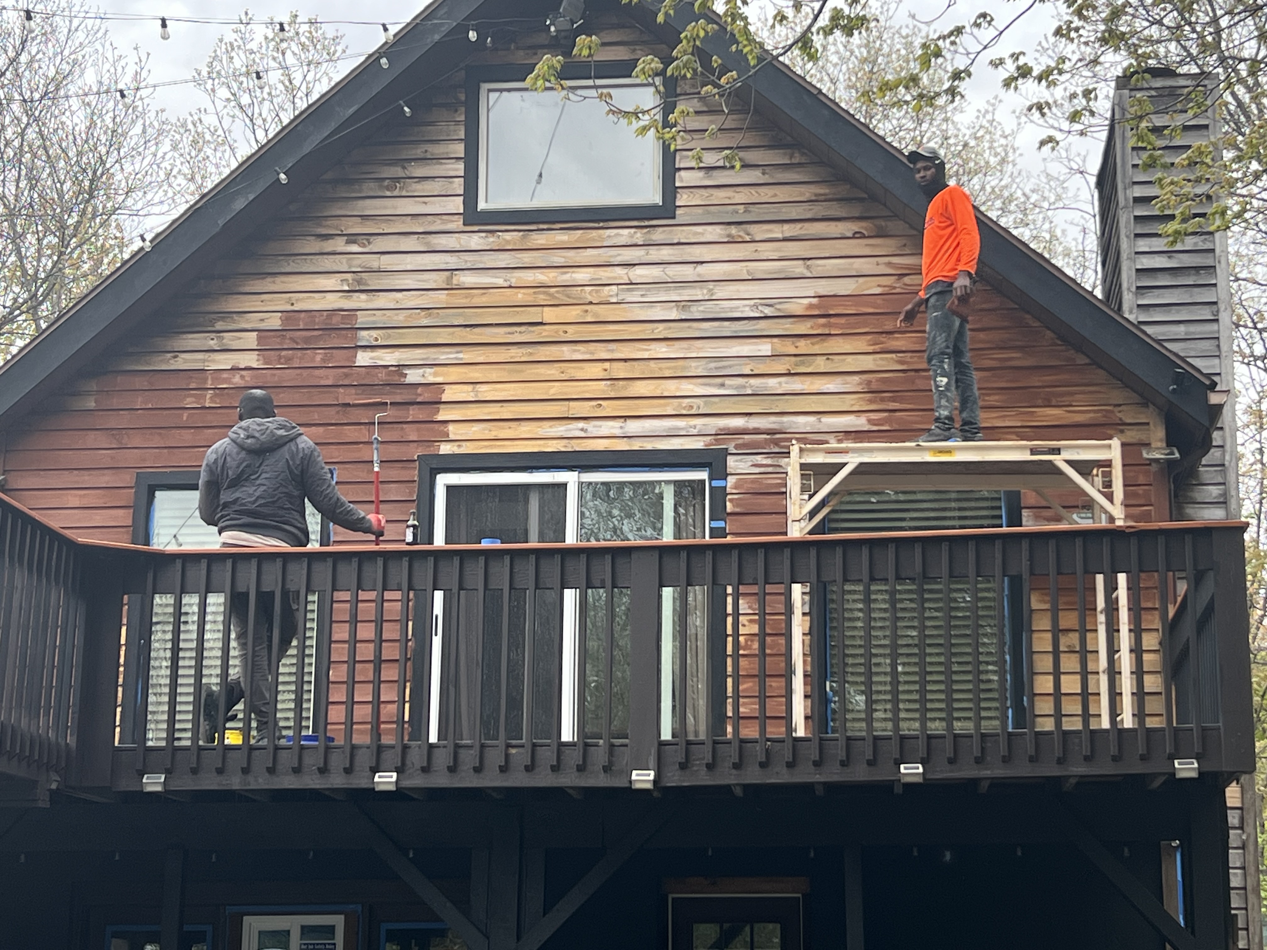 Poconos cabin in progress — two crew members staining the gable end from a scaffold platform