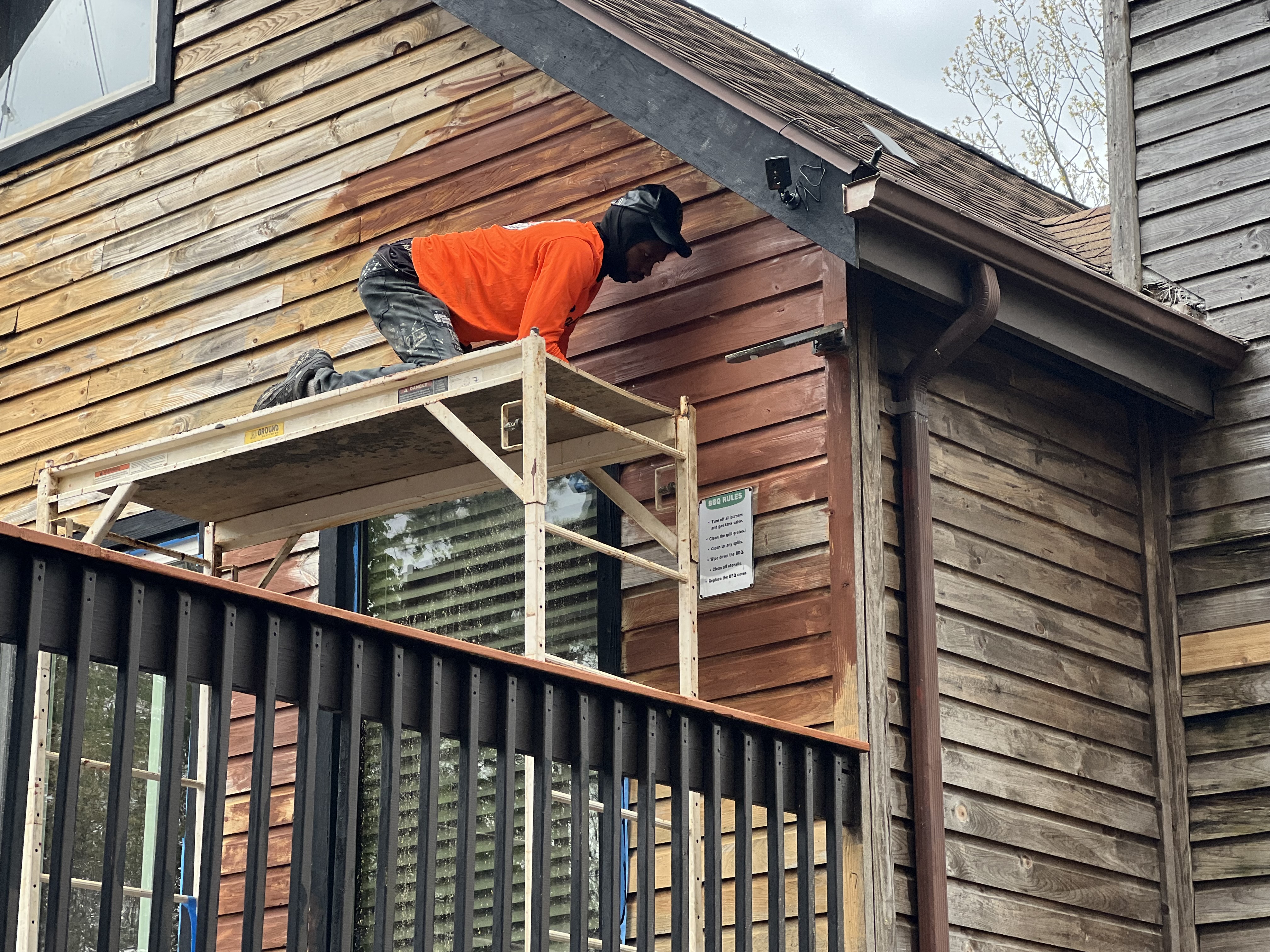Poconos cabin in progress — crew member on scaffold staining upper siding near roofline