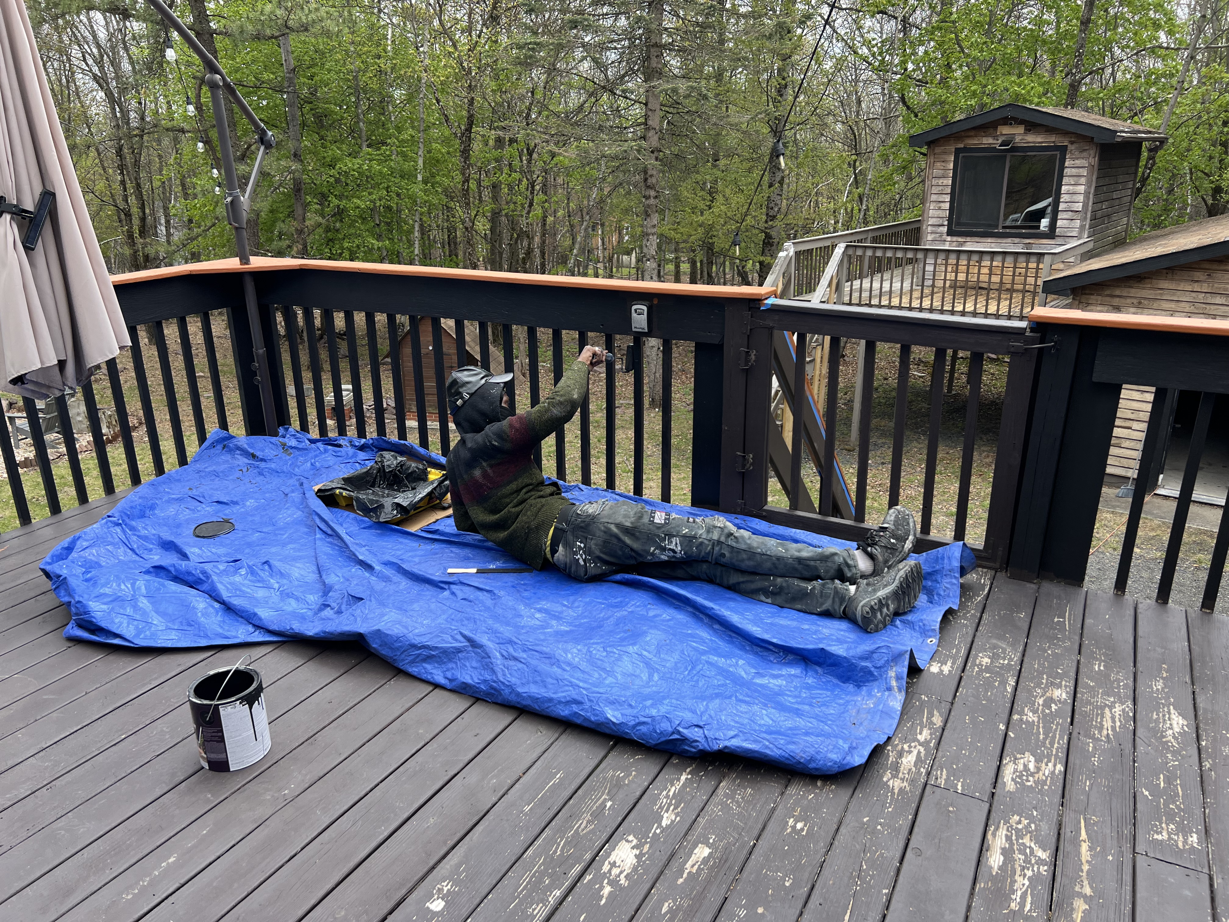 Poconos cabin in progress — crew member working on deck railing detail with protective blue tarp setup
