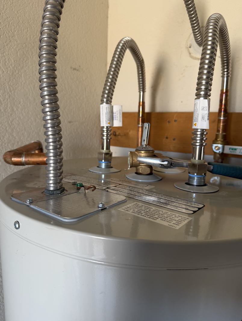 Water heater repair and valve service with stainless steel flex lines and copper fittings on a water heater tank in a Peoria, AZ home