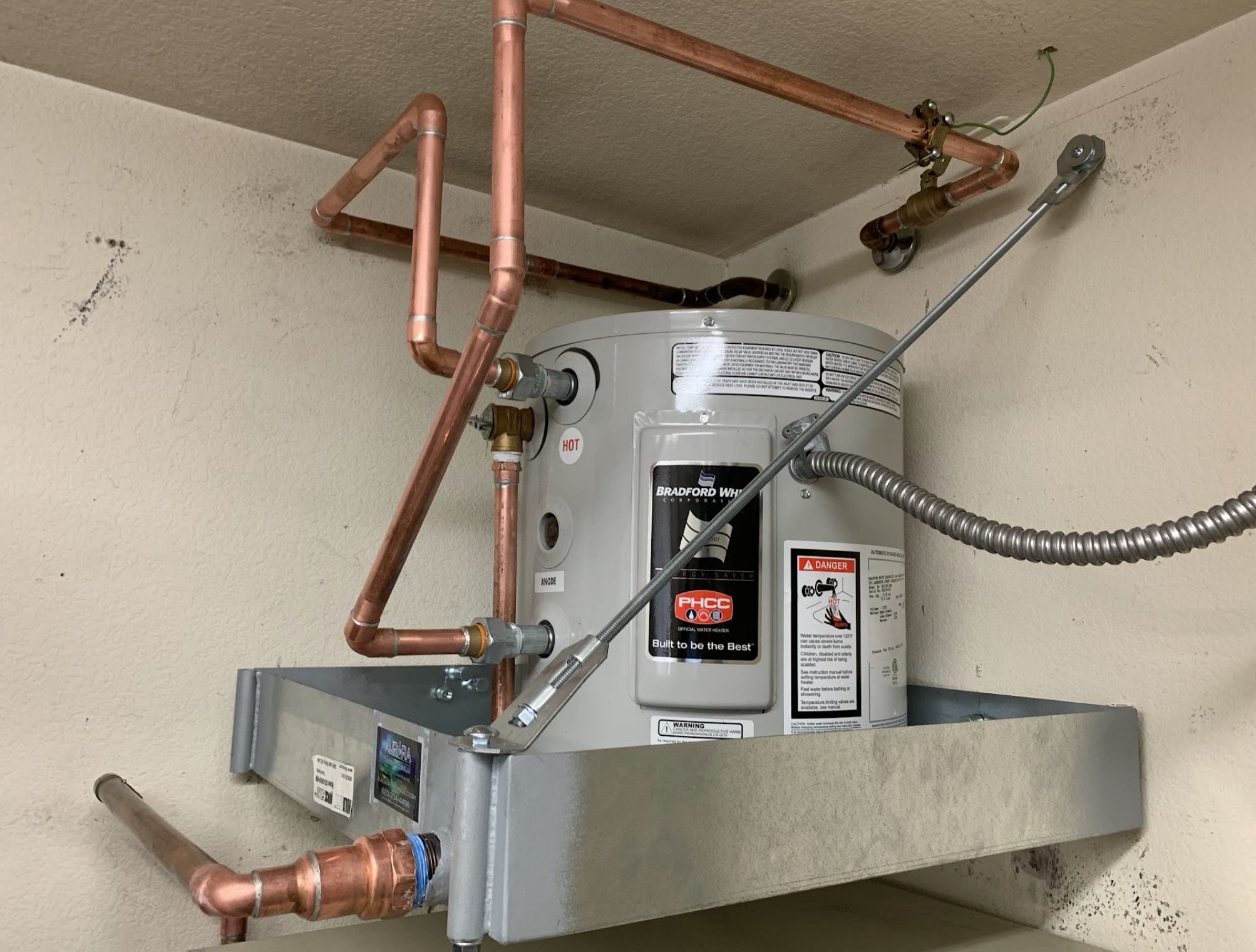 Bradford White compact water heater on a wall-mounted support platform with copper piping installed by Aurora Plumbing & Mechanical