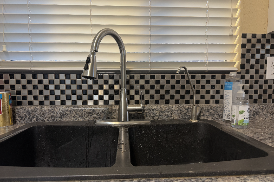 Brushed nickel gooseneck pull-down faucet and drinking water tap installed on a black double-basin kitchen sink during a Peoria remodel