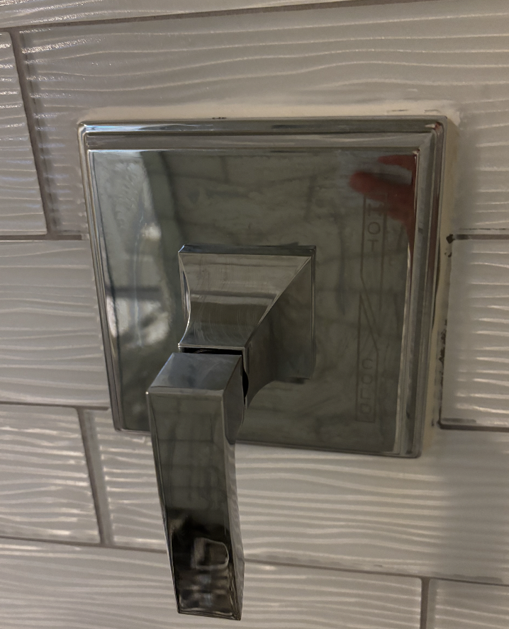 Chrome shower valve handle and trim kit installed on textured white subway tile during a bathroom plumbing repair