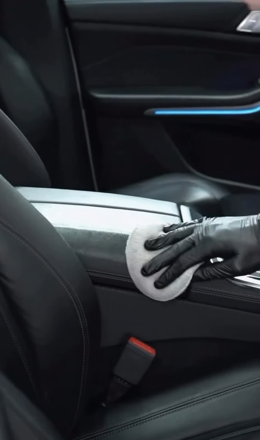 Gloved mobile detailer wiping a vehicle’s center console.