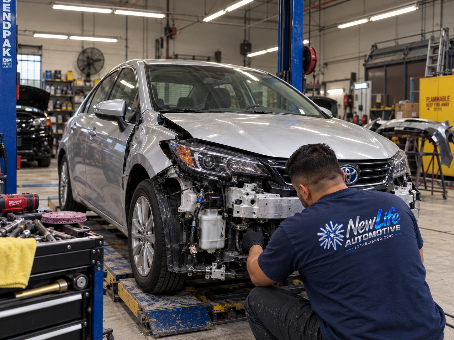 New Life Automotive technician in branded shirt working on front-end collision repair on a vehicle on hydraulic lift at Fullerton, CA repair shop