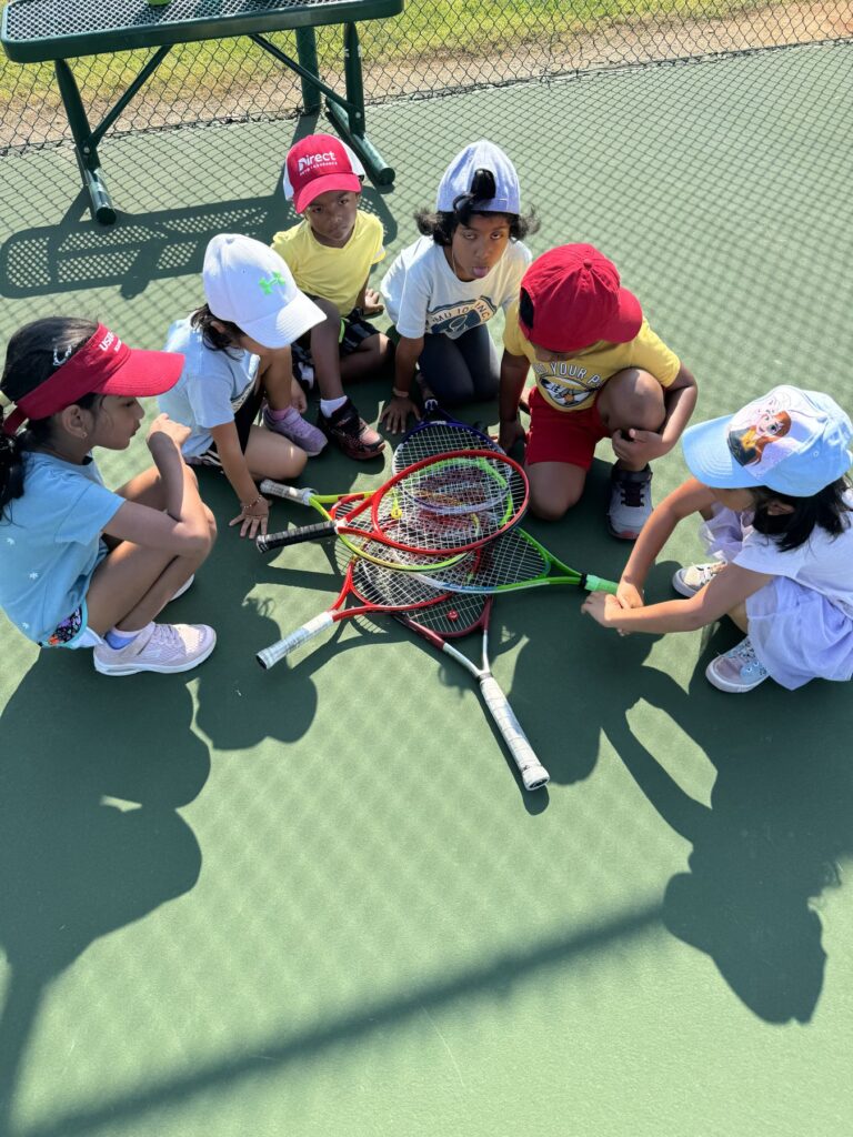 Young tennis kids sitting in a circle on court with rackets stacked in center