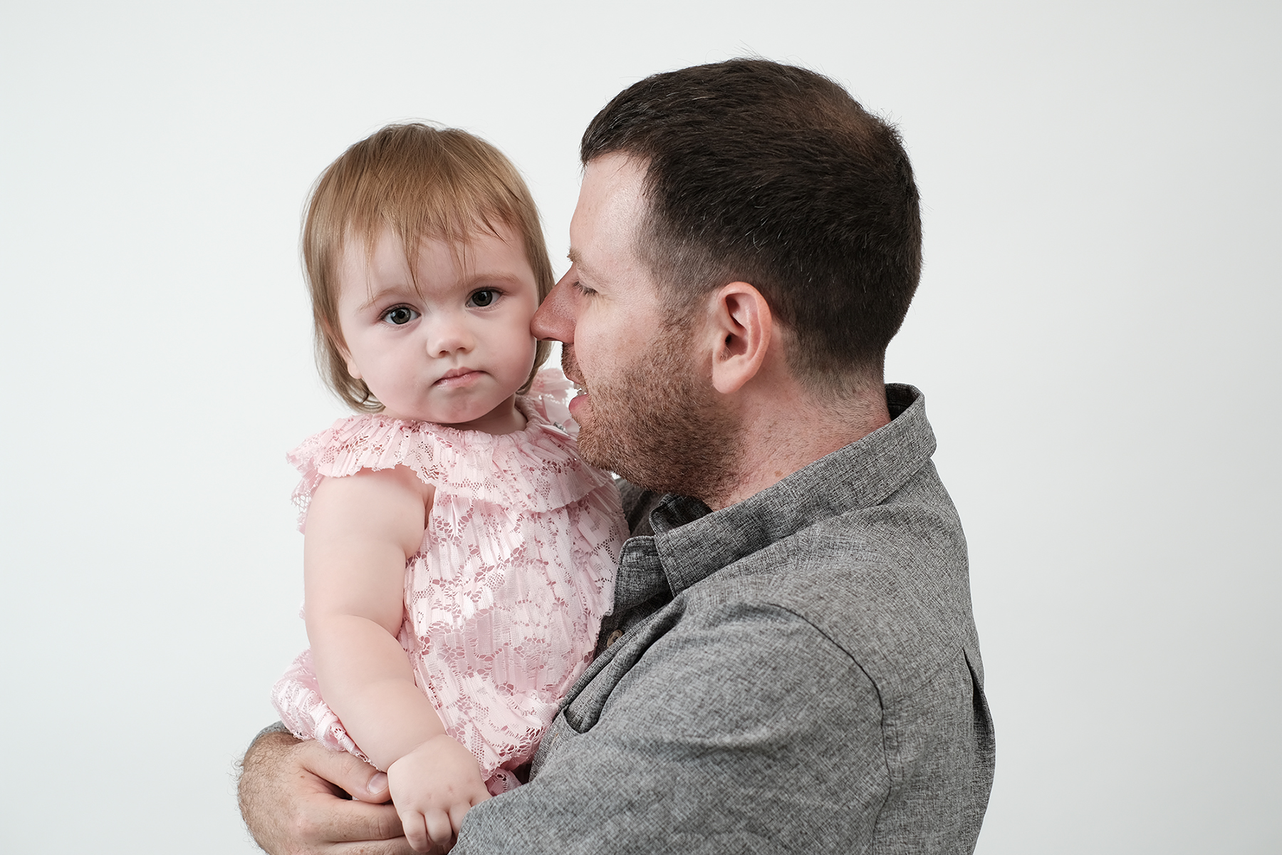 Tender fine art portrait of a father holding his young daughter in a soft pink lace dress