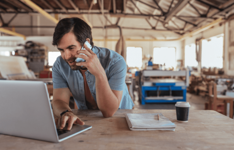 Tradesperson on the phone with laptop in workshop