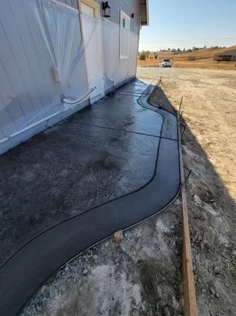 Curved decorative stamped concrete walkway with smooth troweled border along home exterior