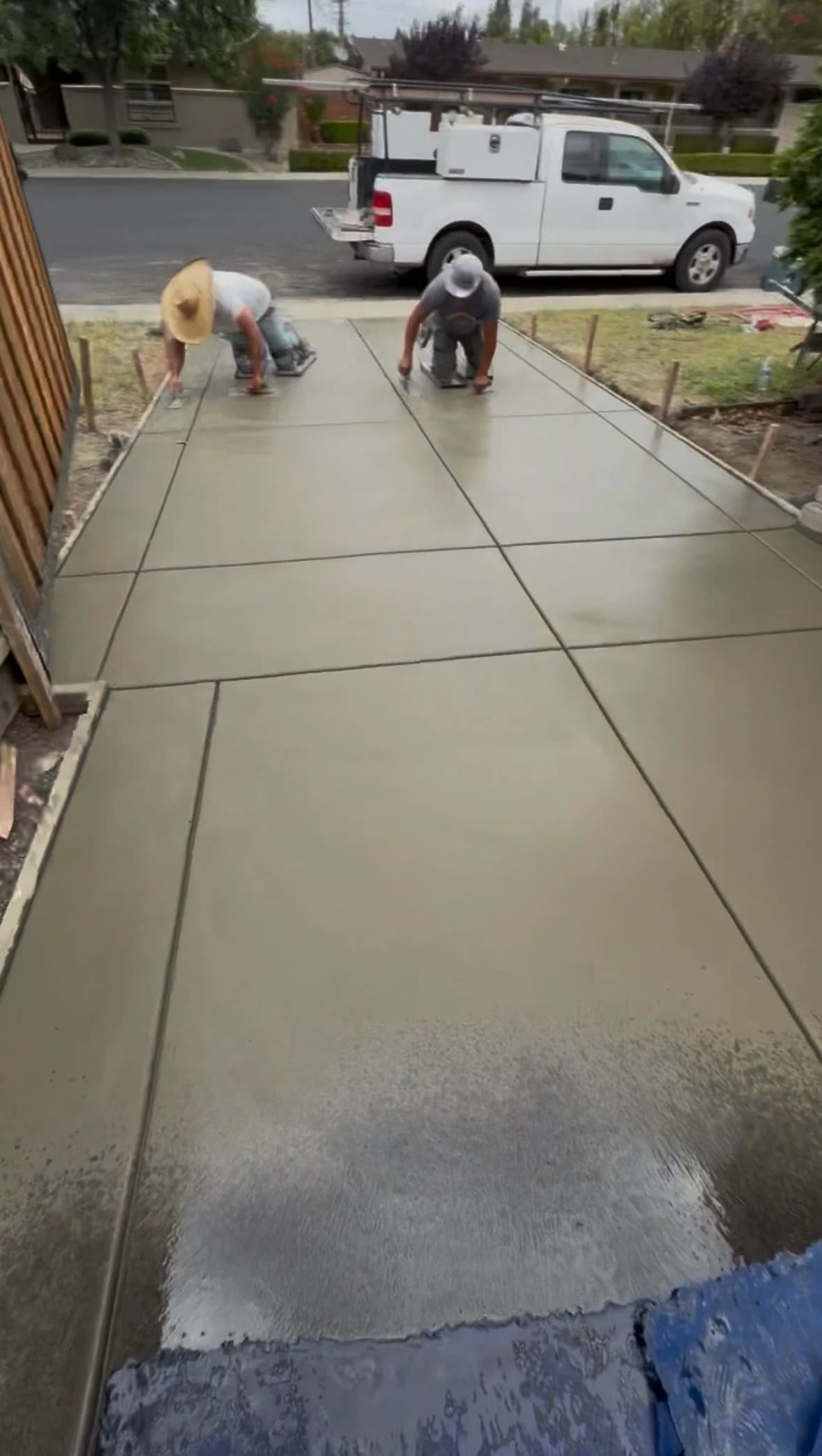 Concrete finishing crew hand-troweling a freshly poured concrete driveway surface