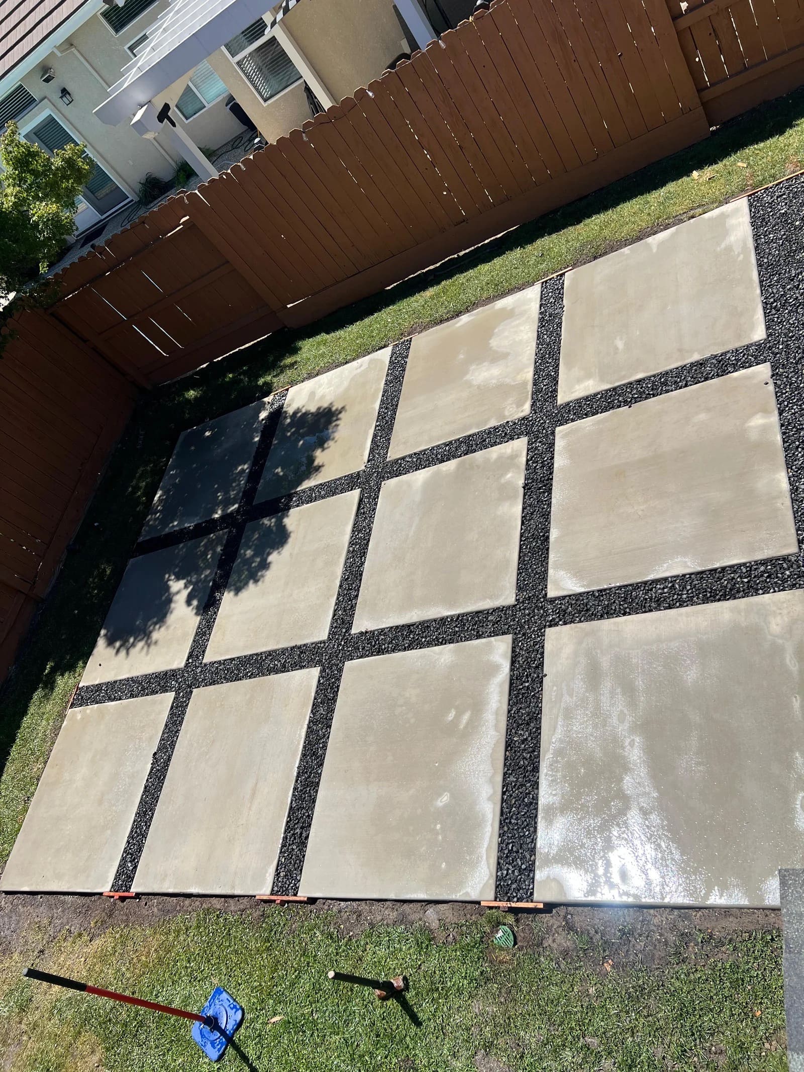 Modern concrete patio slabs separated by black decorative gravel joints in backyard