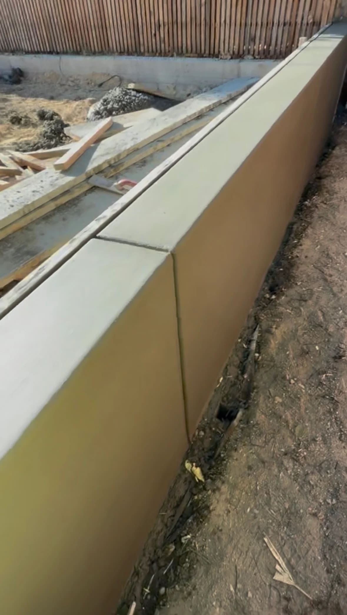 Smooth poured concrete retaining wall along residential fence line