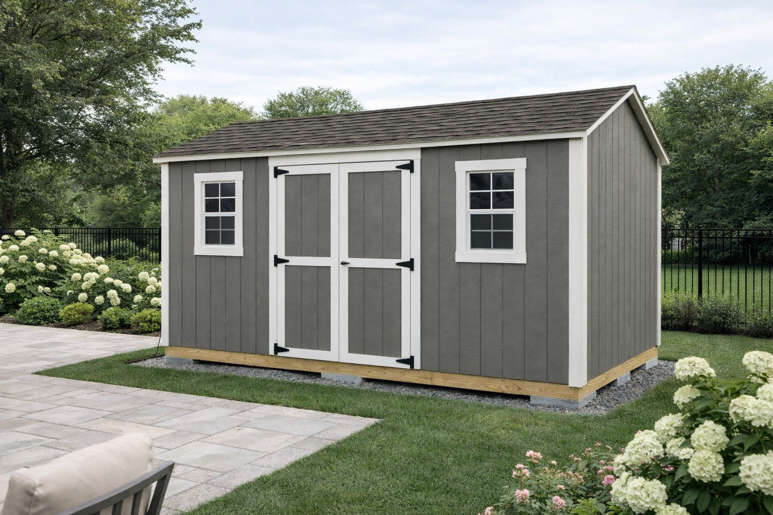 Grey Backyard Shed with white trim, double doors and two front windows beside a patio