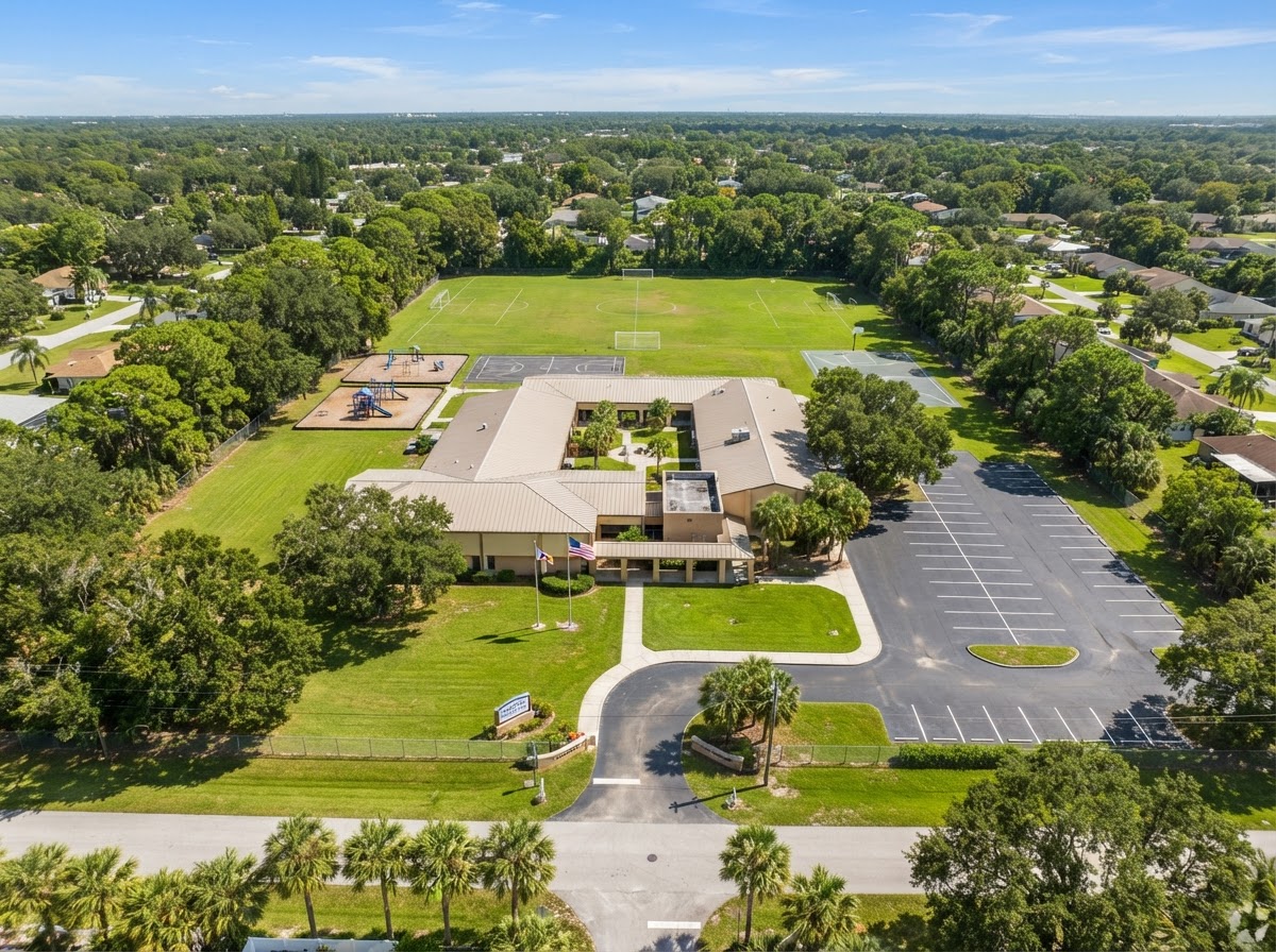 The 1.7 acre Jelly Bean Junction campus with a single story building, grassy play area, and mature trees