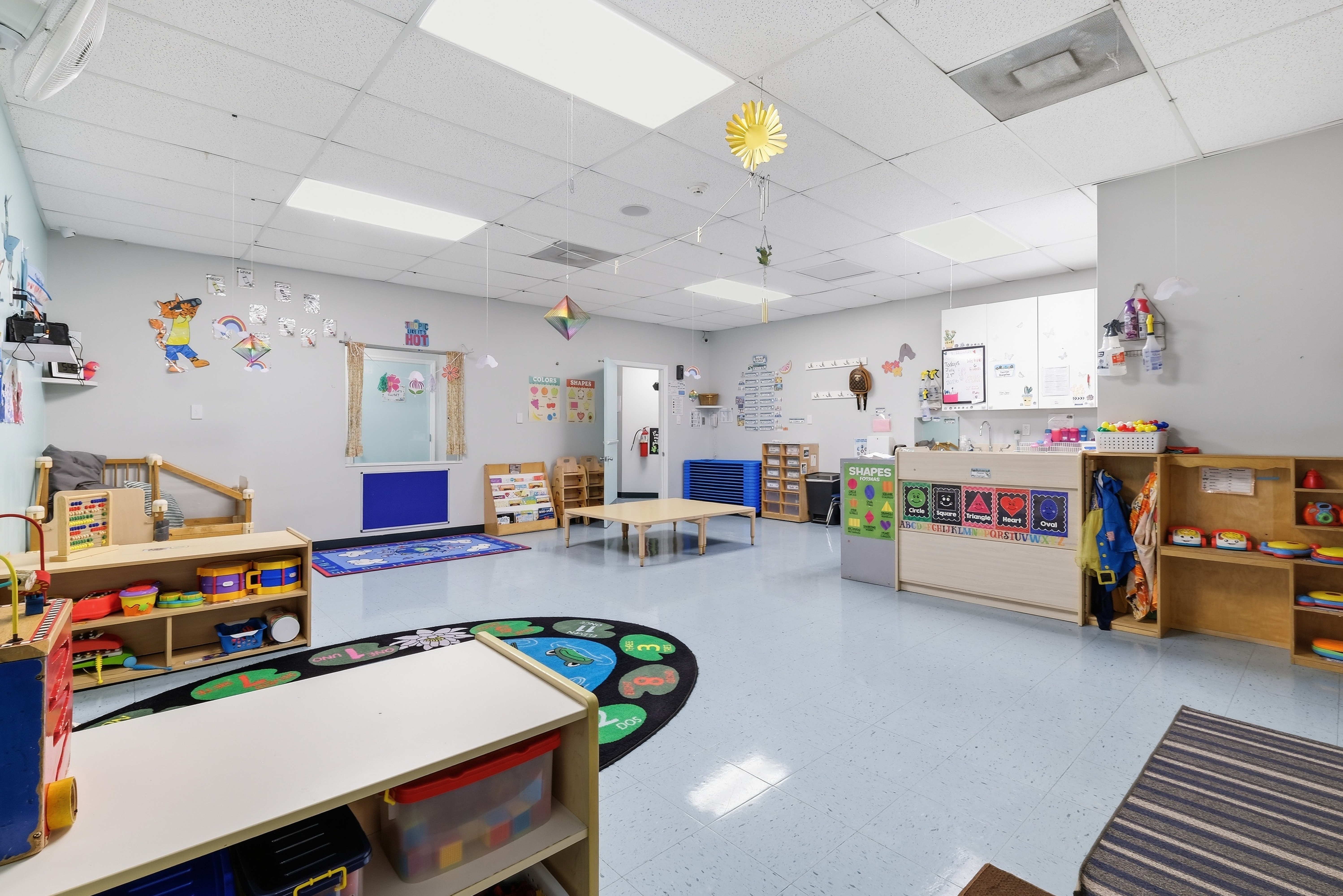 Toddler classroom with low tables, sensory bins, blocks, and a book basket on a soft rug