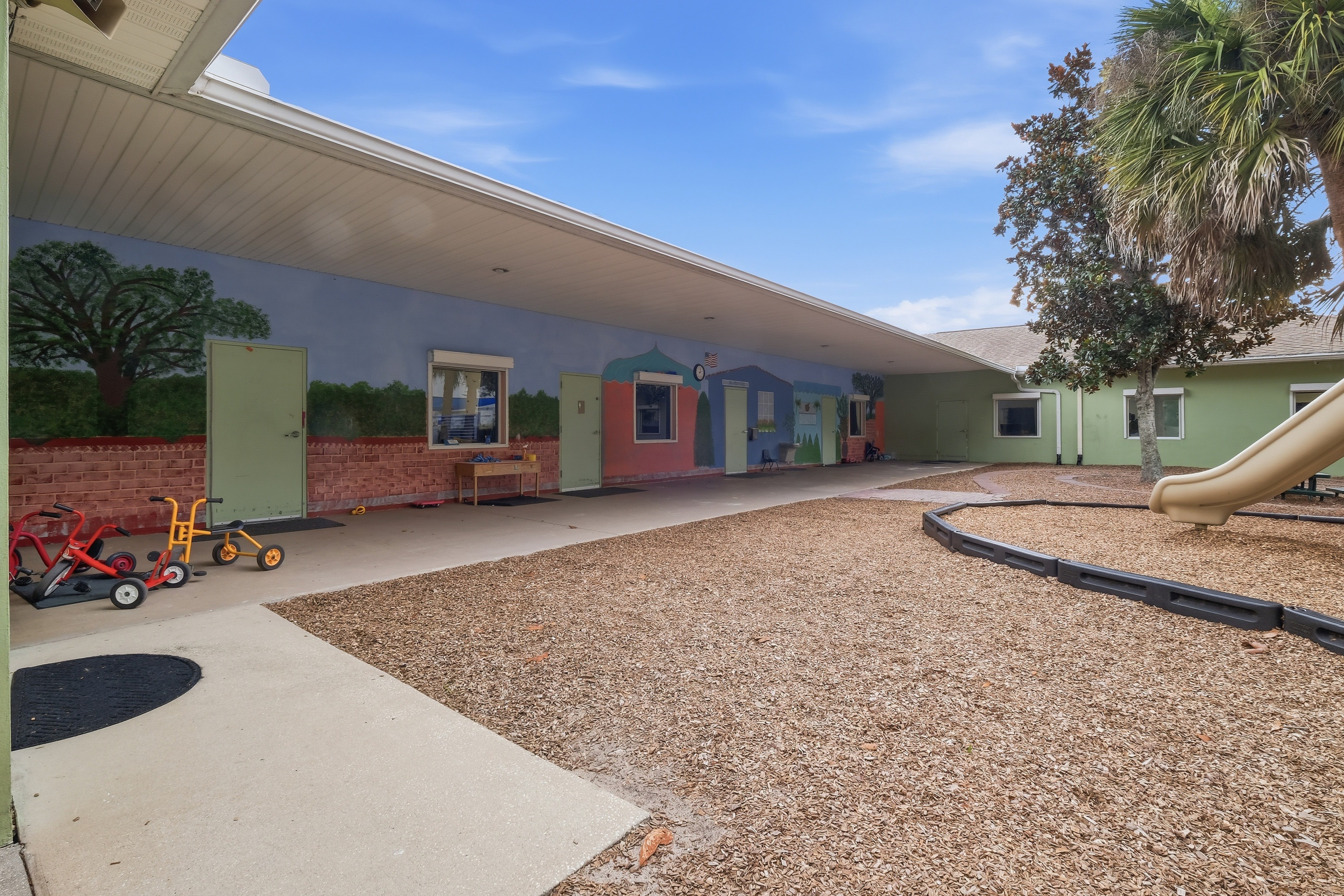 Covered walkway courtyard with painted classroom murals, tricycles, and outdoor play space