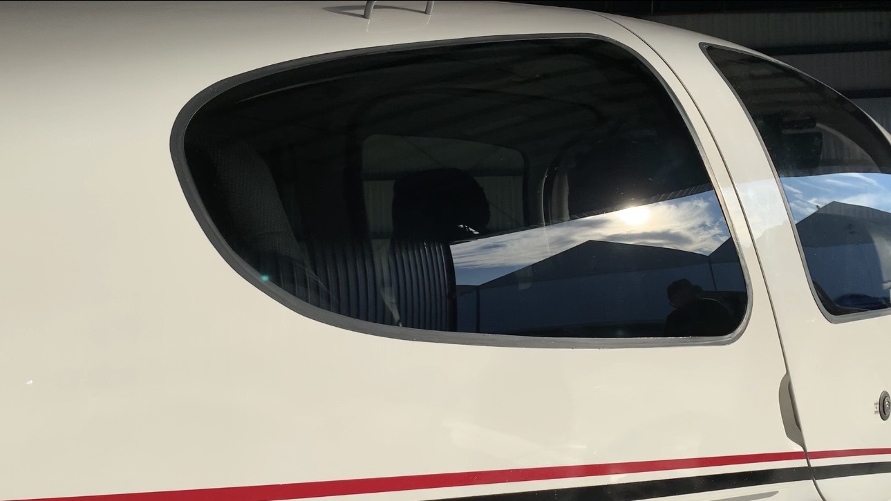 Clean, polished aircraft exterior and cabin window reflecting sky and hangar