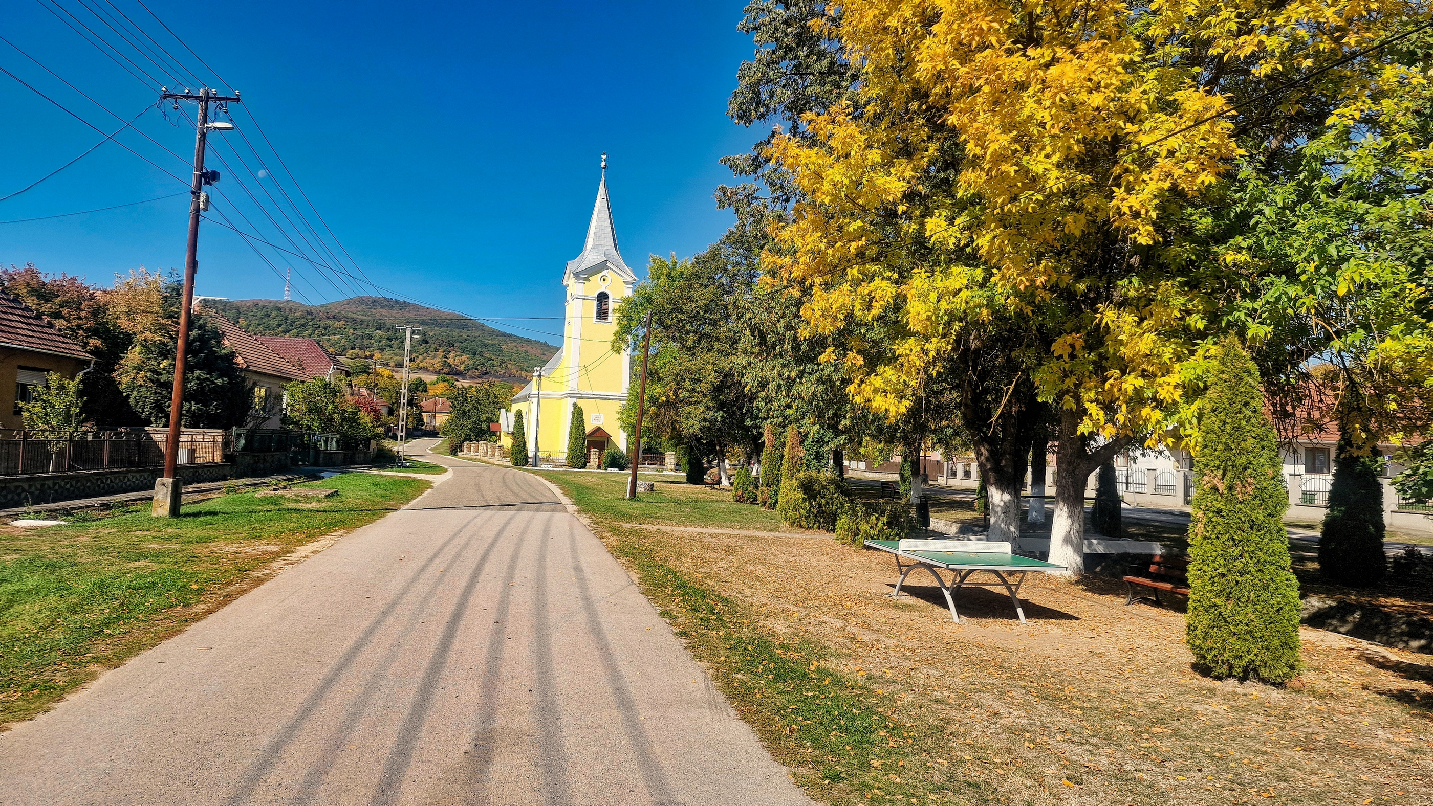 A falu sárga temploma és a központi utcakép az őszi fák között