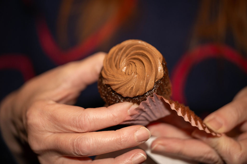 Hands unwrapping chocolate frosted cupcake