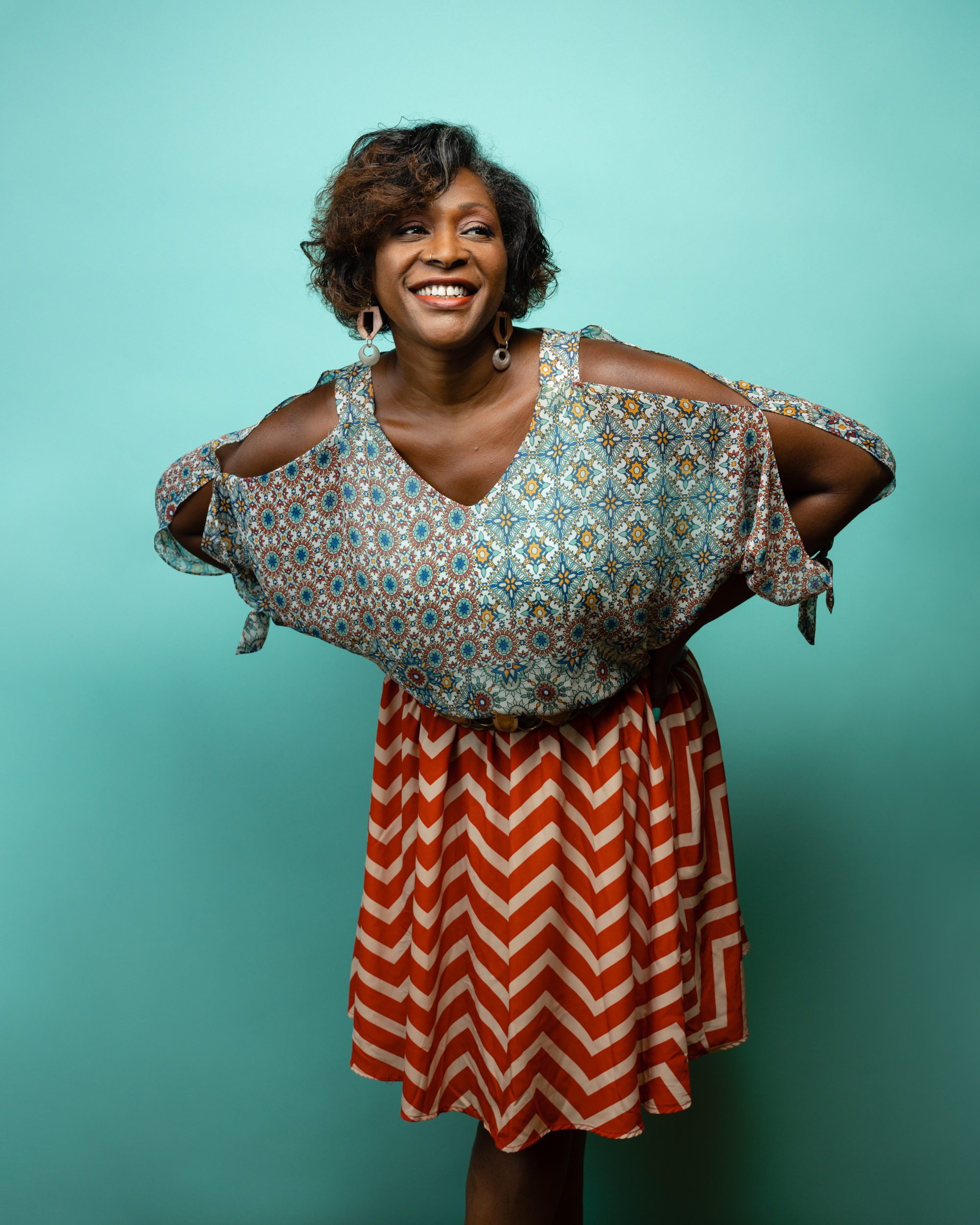 Dasha Kelly smiling in vibrant dress against teal background