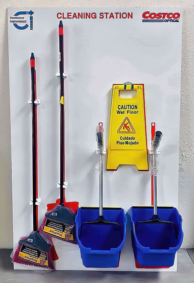 Costco Optical Cleaning Station with Continuous Improvement emblem, dual red and blue brooms, upright dustpans, and Caution Wet Floor sign bracket