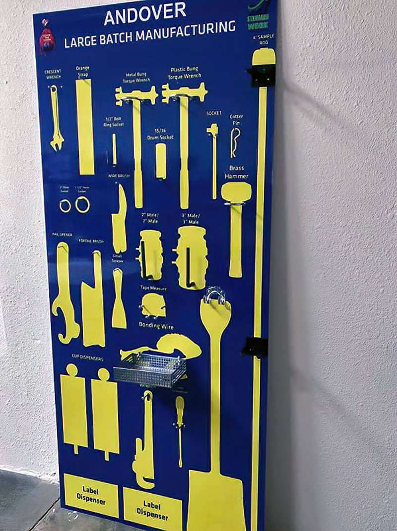 Sherwin-Williams Andover Large Batch Manufacturing royal blue tool shadow board with high-visibility yellow silhouettes for bung torque wrenches, sockets, brass hammer, and label dispensers