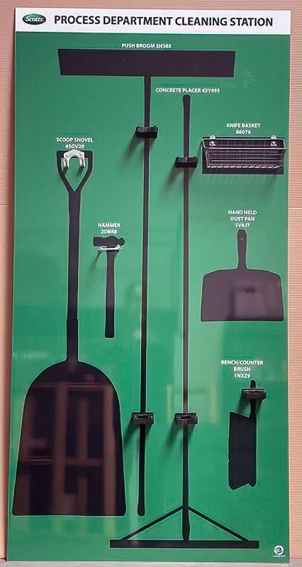 Scotts Process Department Cleaning Station green shadow board with black silhouettes for push broom, concrete placer, knife basket, scoop shovel, hammer, and dustpans