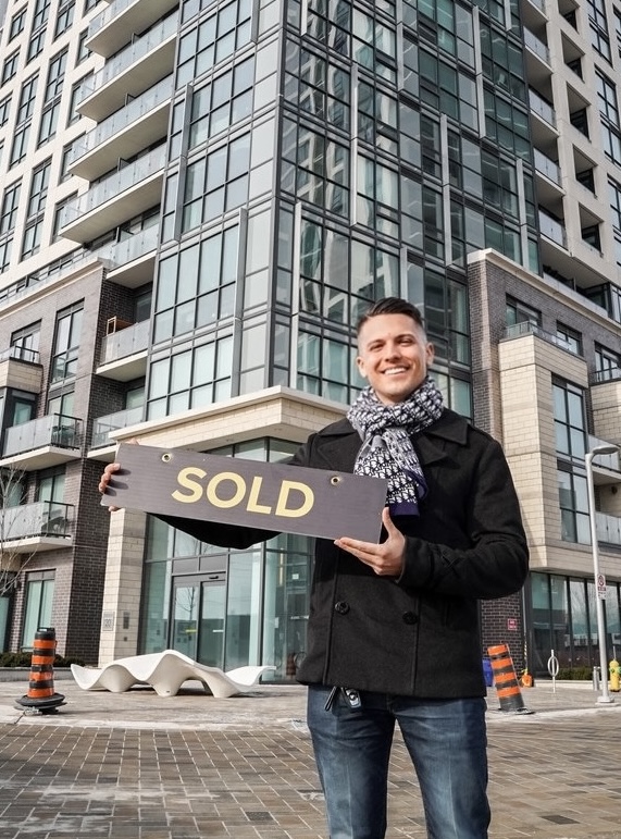 Christian Moretuzzo holding a SOLD sign outside condo building