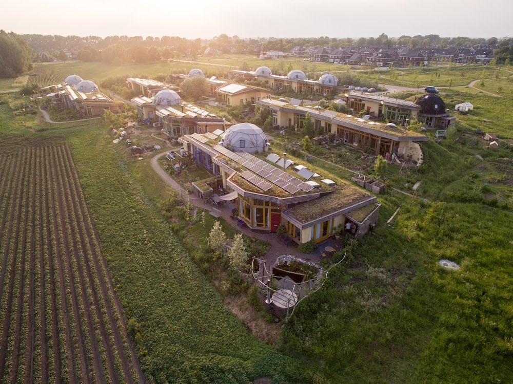 Comunidad ecológica integrada con domos, techos verdes vivos, huertos y paneles solares al atardecer.
