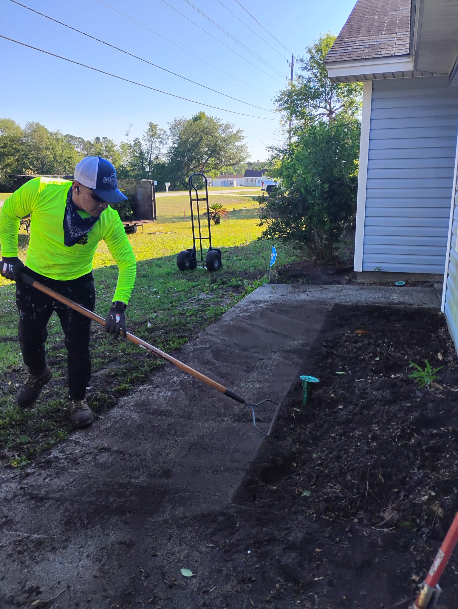 Worker raking soil and cleaning sidewalk after tree service work in Brunswick Georgia