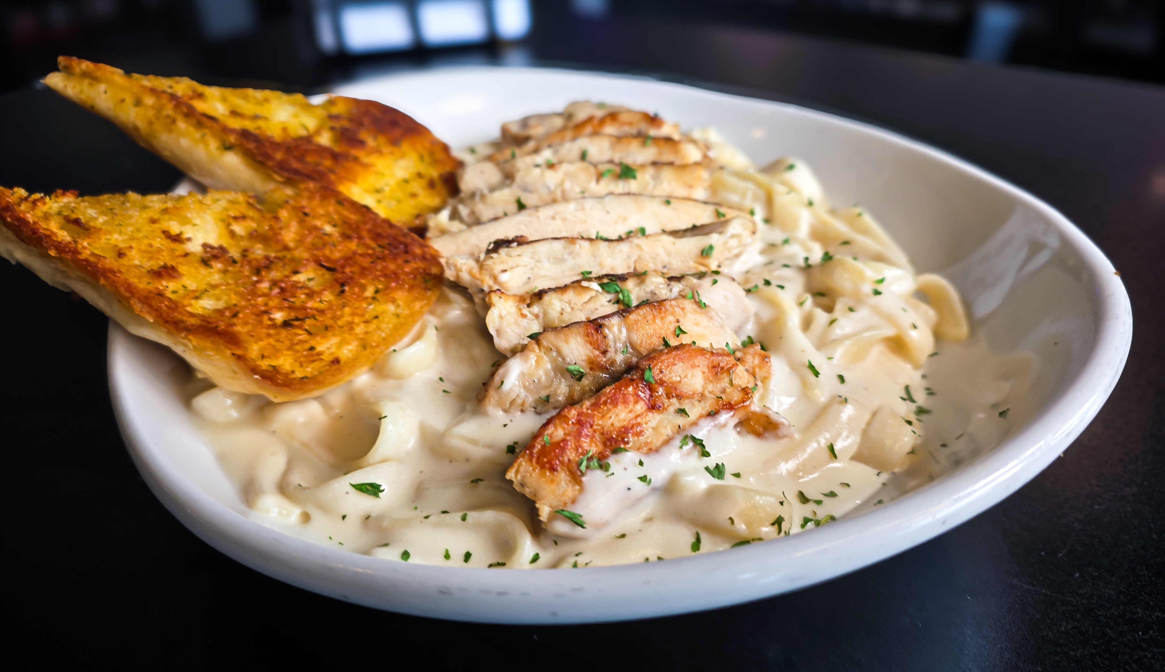 Creamy fettuccine pasta topped with sliced grilled chicken breast and toasted garlic bread