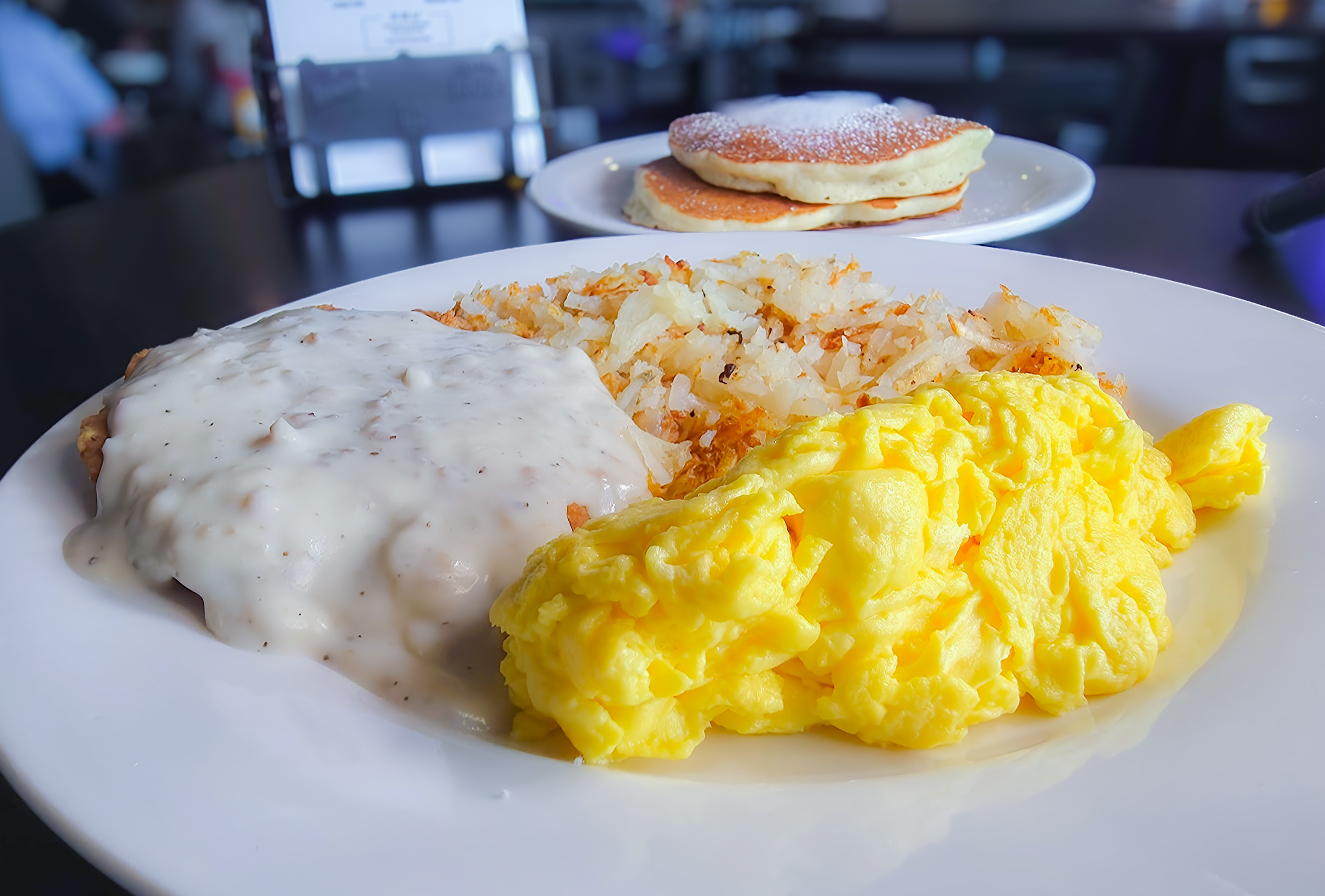 Hearty breakfast platter featuring country fried steak smothered in sausage gravy, scrambled eggs, hash browns, and pancakes