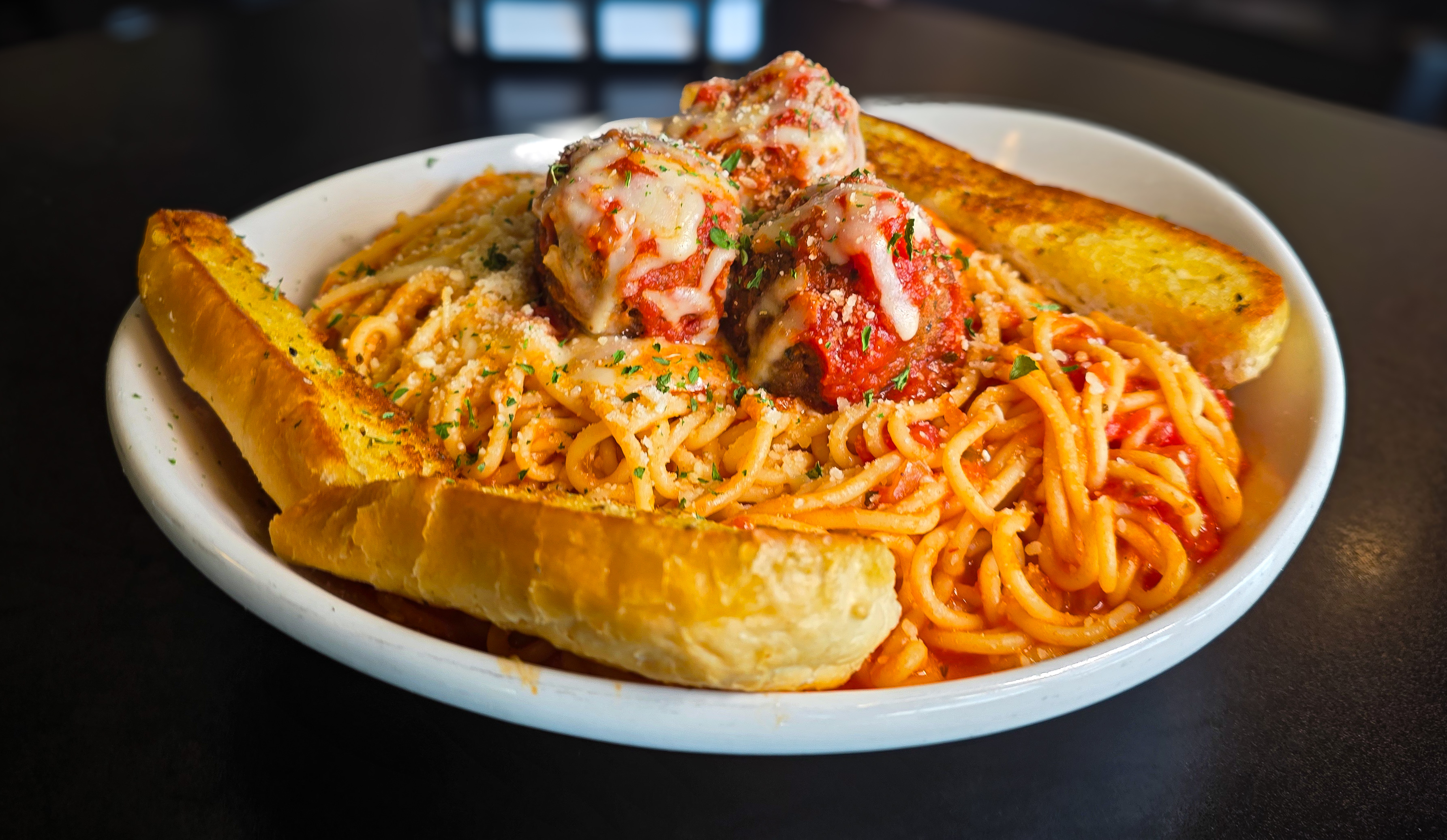 Hearty bowl of Italian spaghetti pasta with large meatballs melted mozzarella cheese and crispy garlic toast