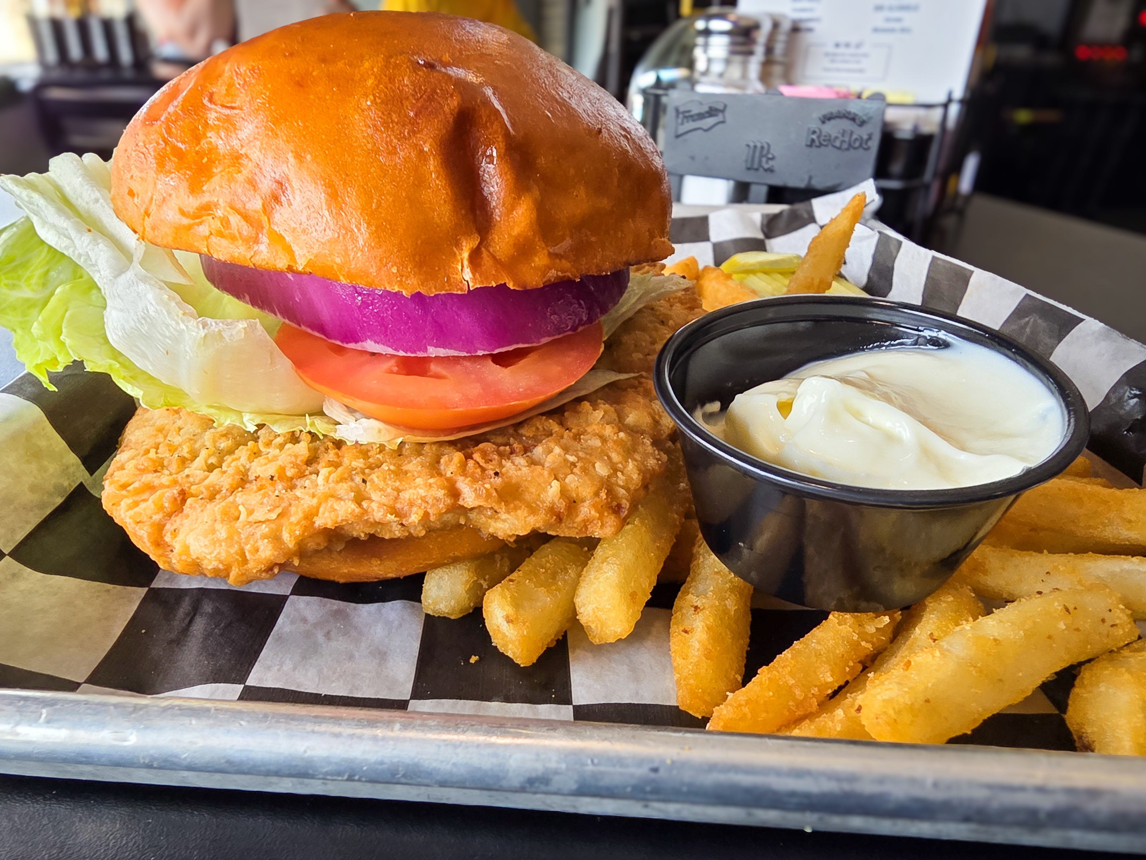 Crispy golden hand-breaded pork tenderloin sandwich with red onion lettuce tomato and fries