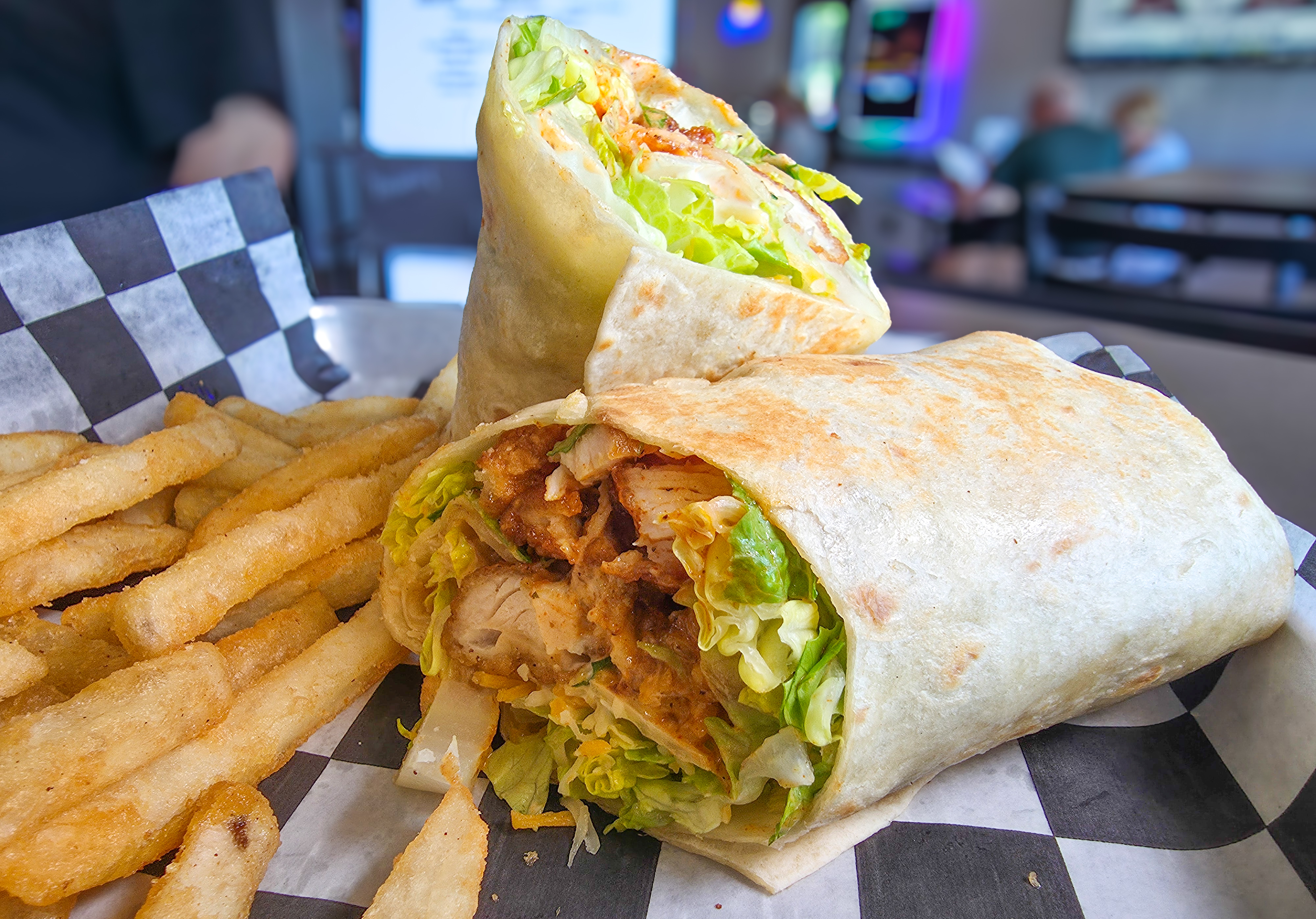 Jumbo tortilla wrap sliced in half filled with golden chicken tenders crisp lettuce and cheddar cheese served with fries