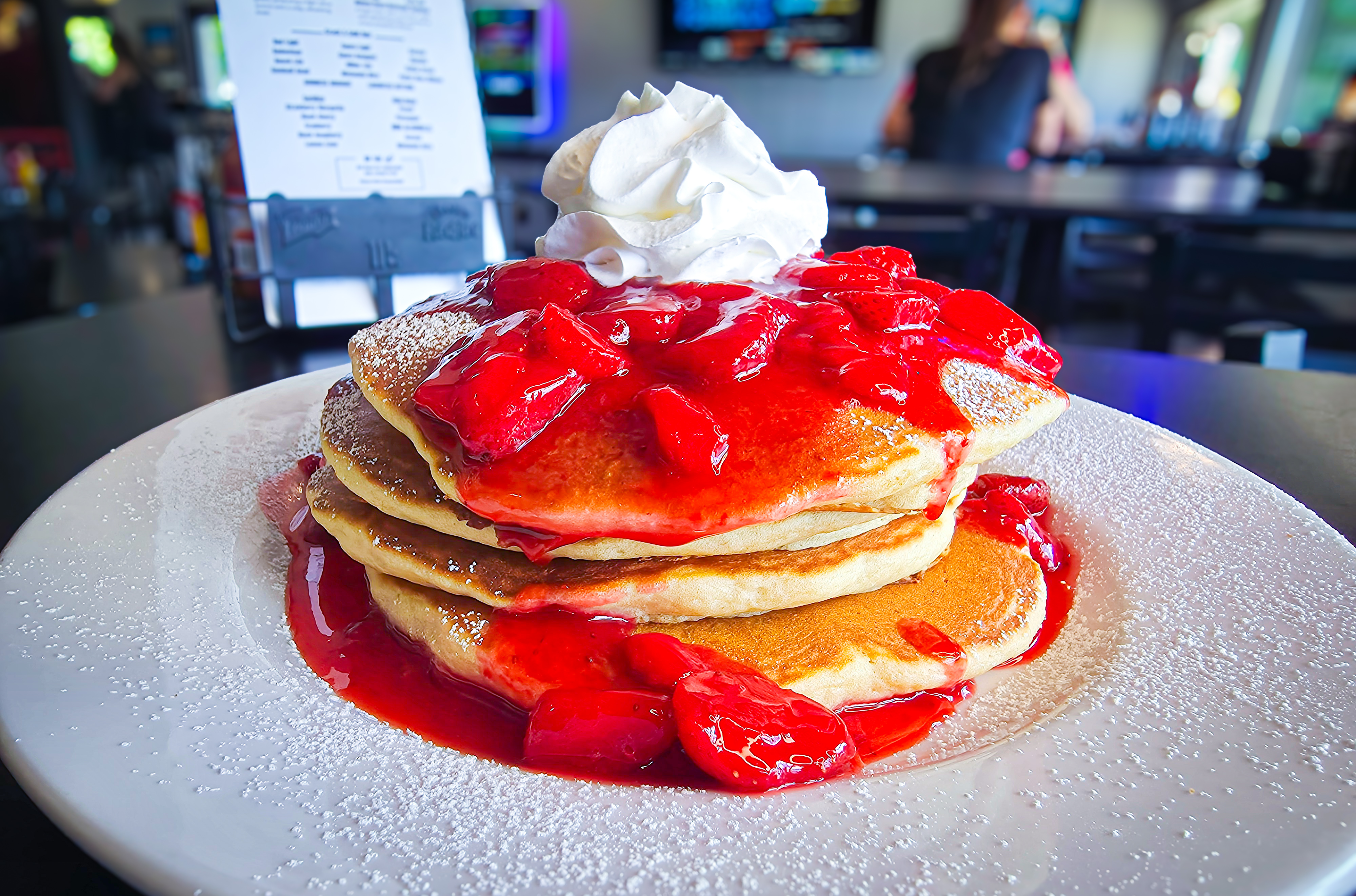 Fluffy griddled buttermilk pancakes topped with glazed strawberries, powdered sugar, and whipped cream