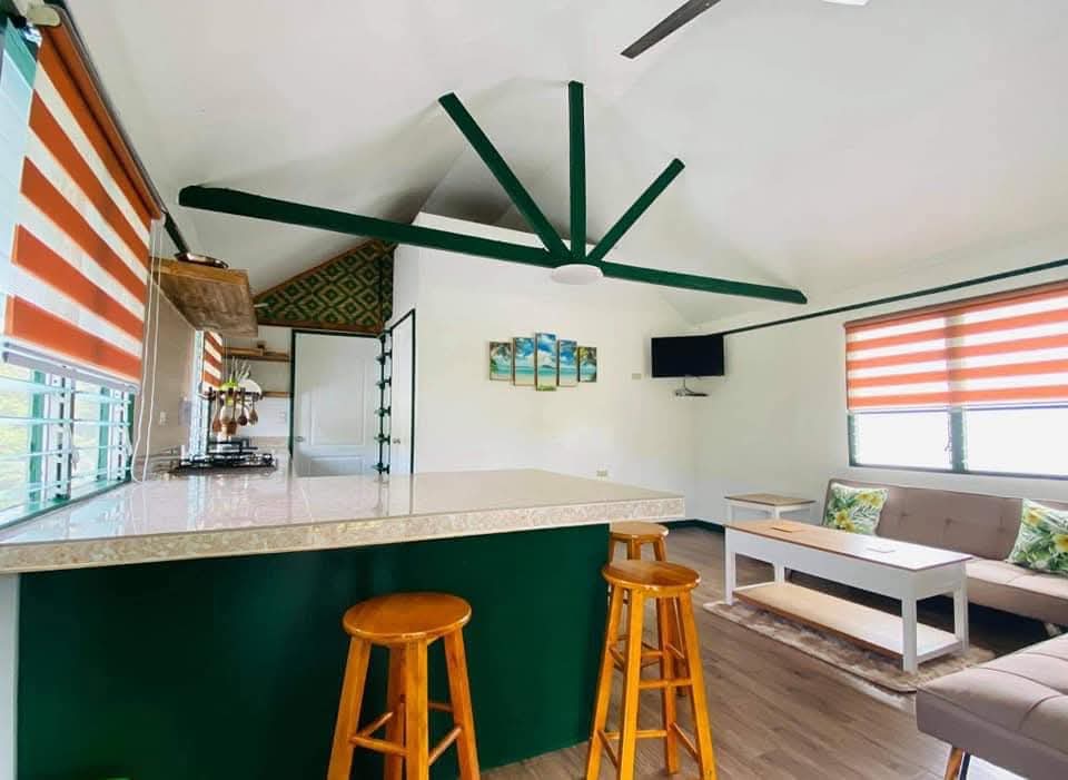 Bright living space at Mims House Cebu with soaring cathedral ceilings, emerald green timber support beams, island counter with wooden barstools, and comfortable seating