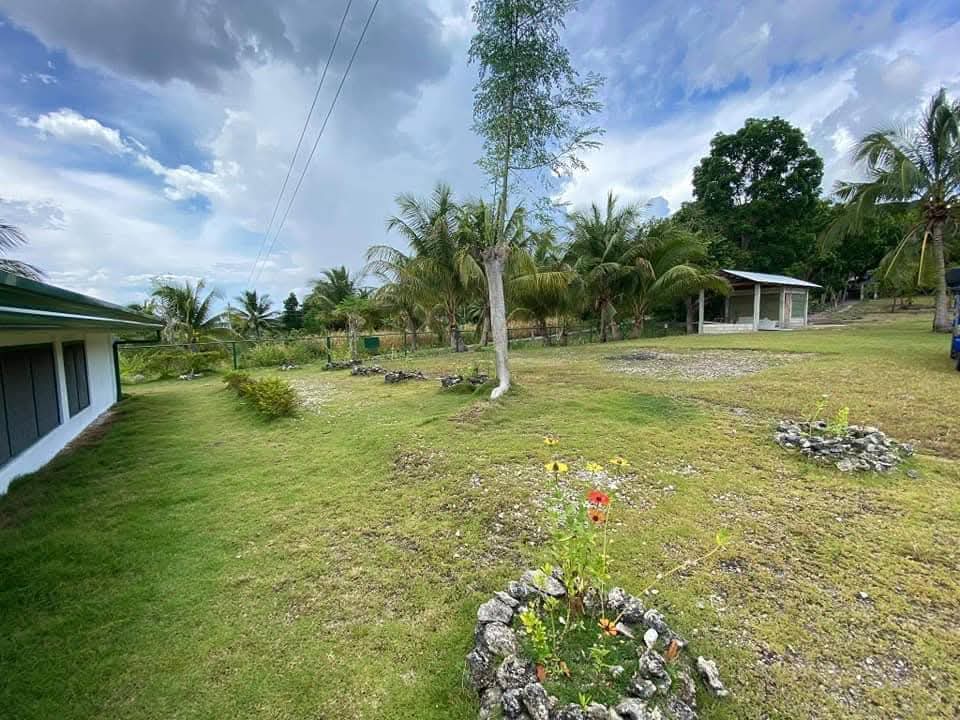 Spacious grassy grounds with stone flower rings, trees, and sky at Mims House Cebu in Samboan
