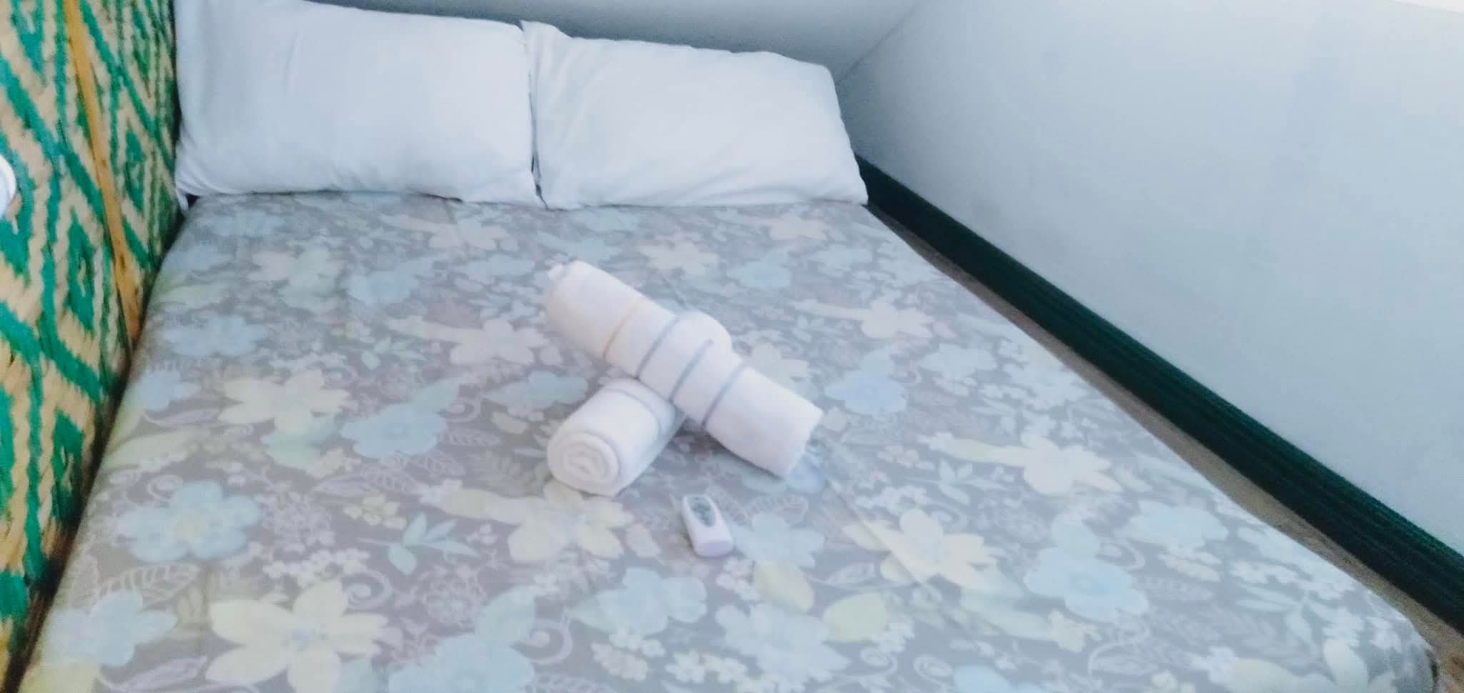 Queen bed with soft floral print bedding, plush pillows, woven amakan accent headboard, and fresh rolled towels at Mims House Cebu