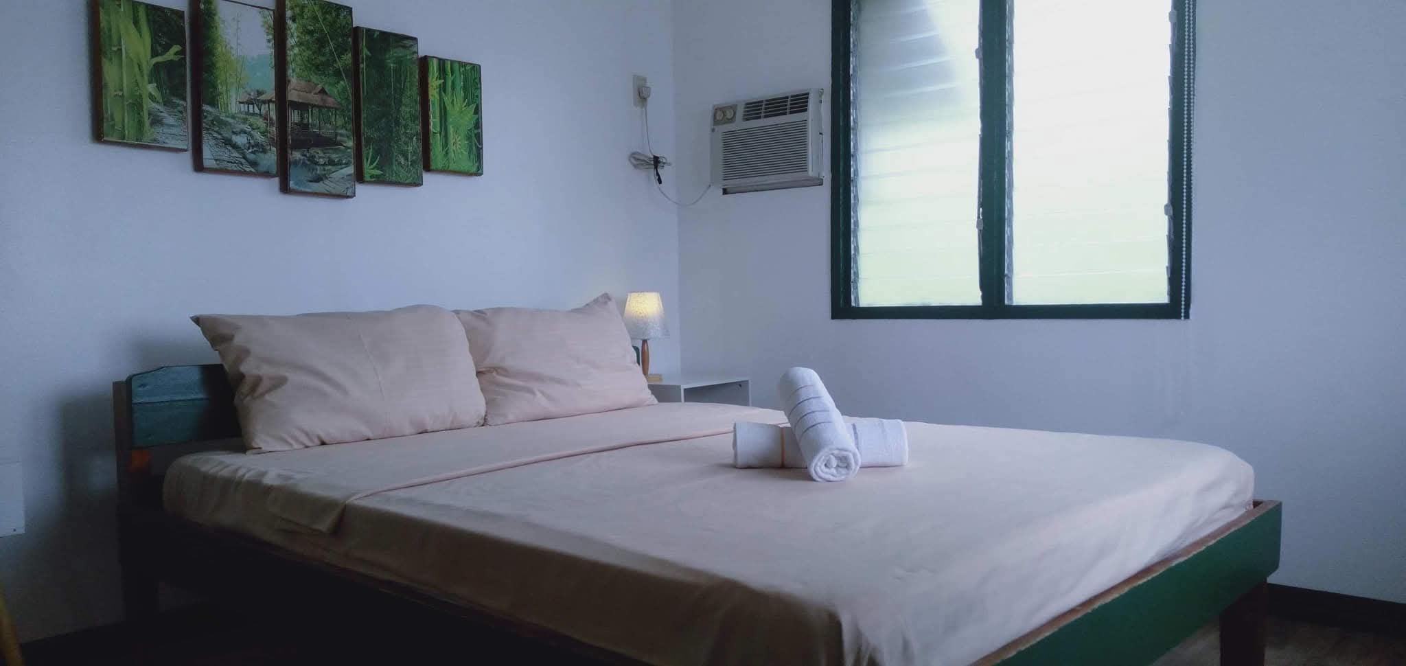 Crisp queen bedroom at Mims House Cebu featuring wall air conditioning, side lamp, forest wall panels, and rolled bath towels
