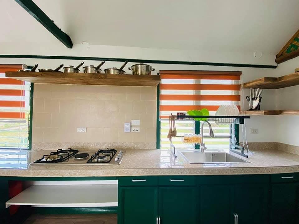 Fully equipped kitchen with dark green cabinetry, gas stovetop, and open wood shelving at Mims House Cebu