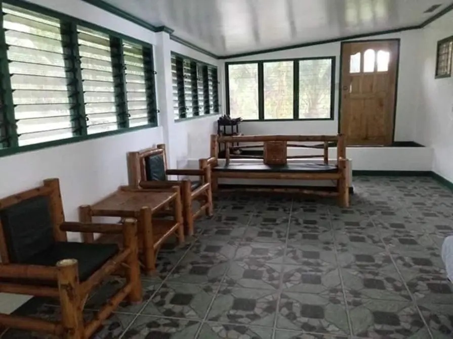 Living room seating area with handcrafted bamboo chairs, natural daylight through louvered windows, and tiled floors