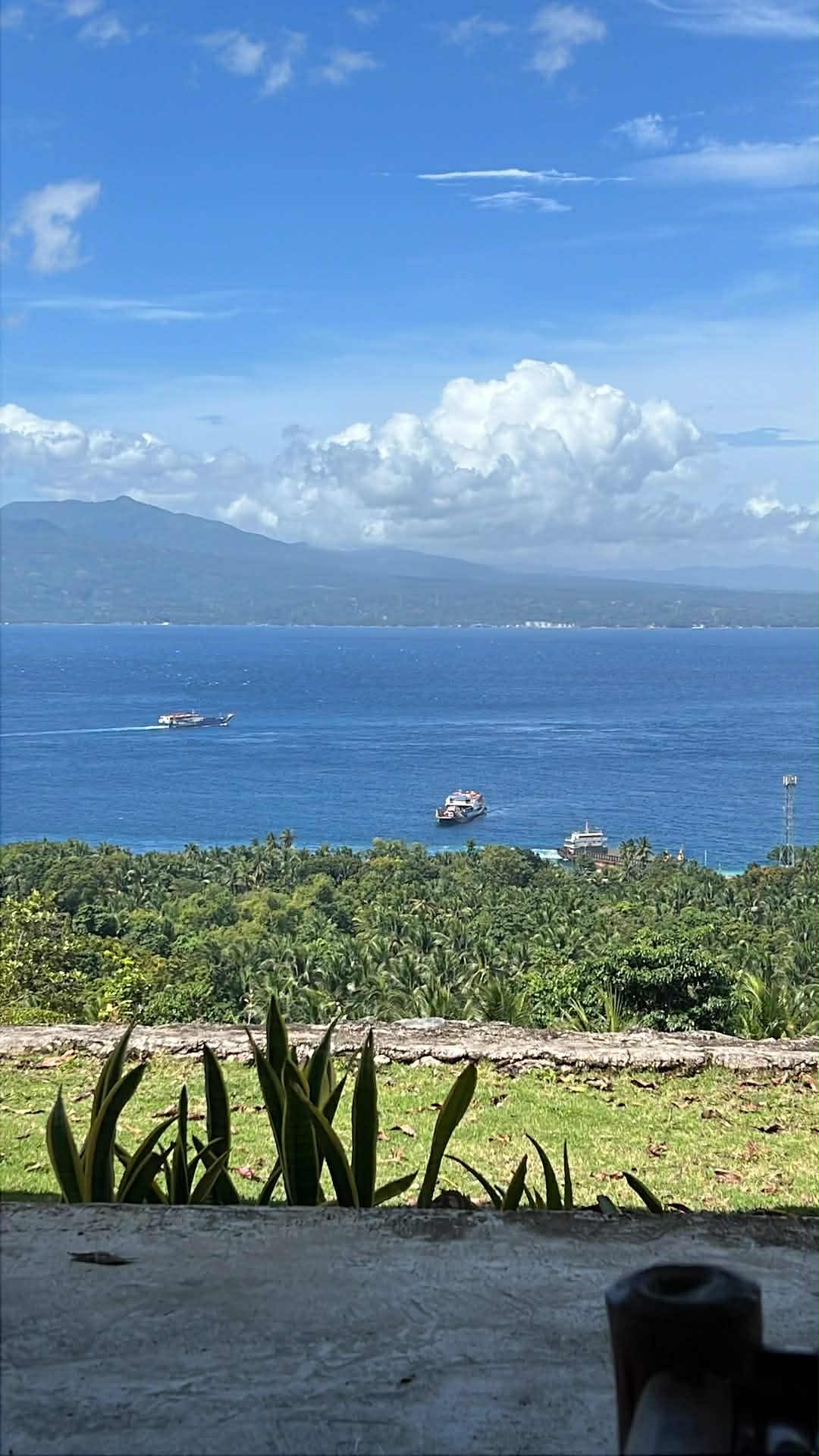 View from Mims House Cebu across potted plants and stone wall out to deep blue sea, passenger ferries, and mountain coastline