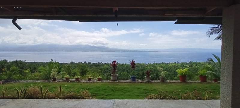 Wide panoramic vista of the calm blue sea and distant island mountain peaks framed under the veranda roofline with potted plants