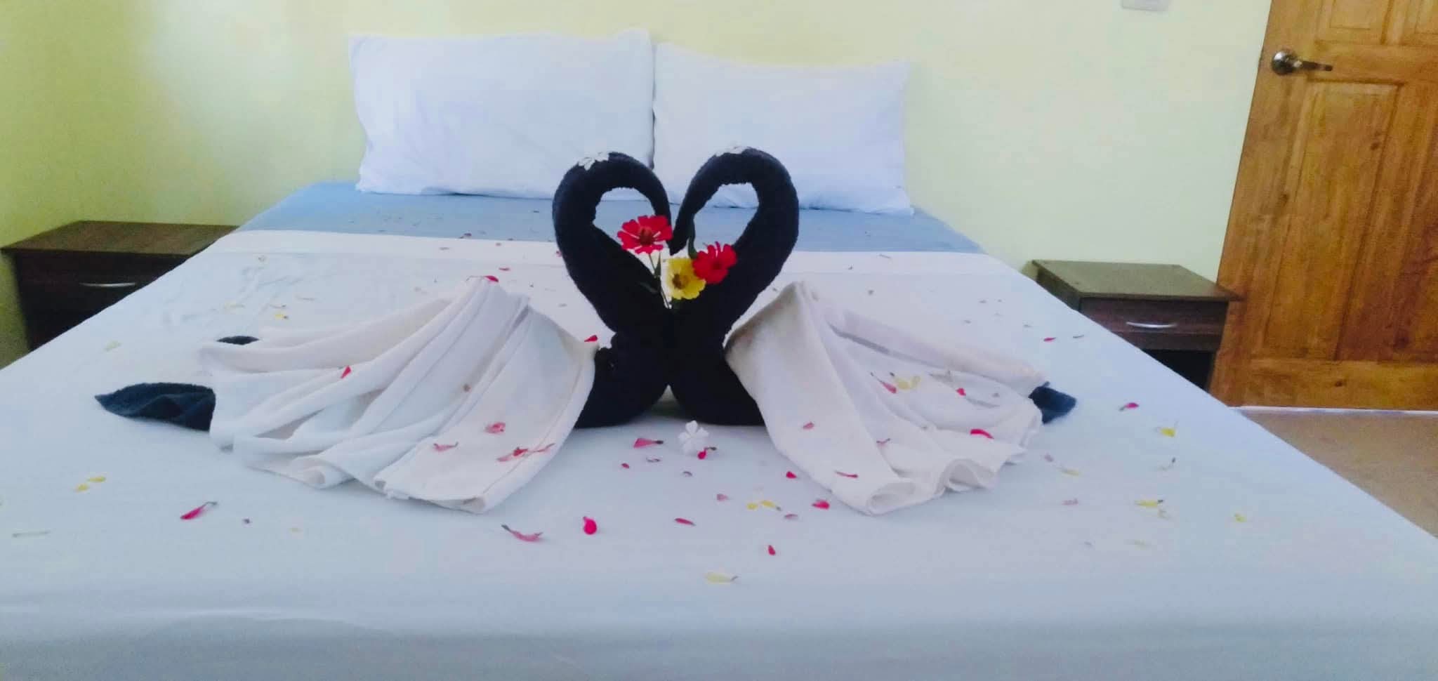Decorative towel swans in heart formation with flower petals on bed at Mims House Cebu