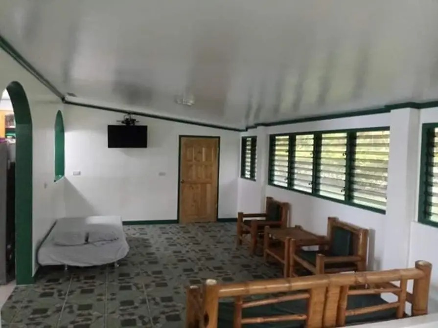 Spacious living room at Mims House Cebu with bamboo seating, wall-mounted TV, tiled floors, and shuttered windows